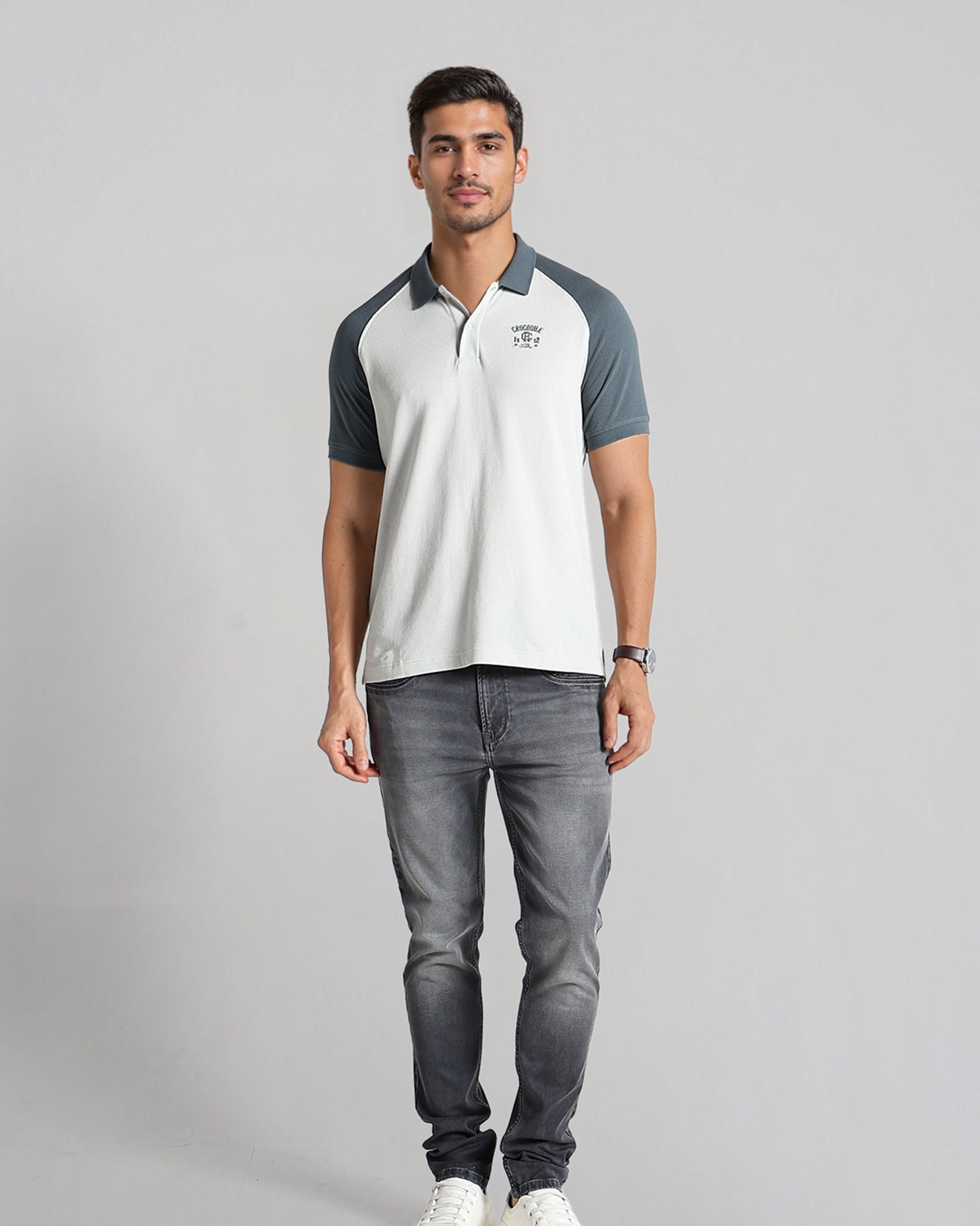 Man wearing a white and gray polo shirt with gray jeans on a light gray background