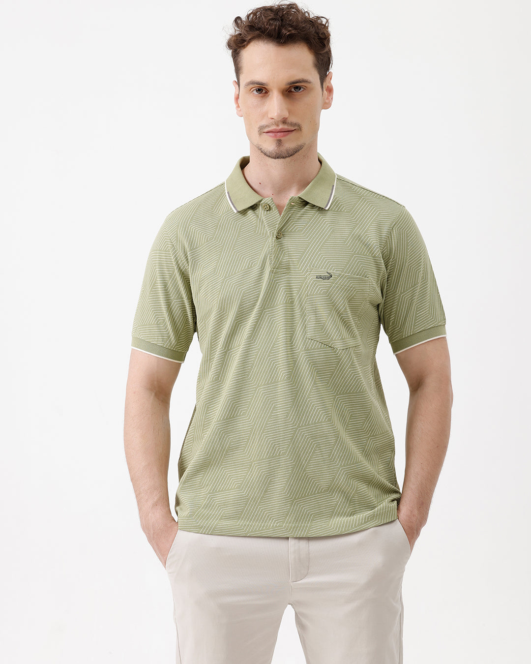 A man wearing a light sage green short-sleeve polo shirt with a subtle geometric pattern, paired with beige trousers, standing against a plain white studio background.