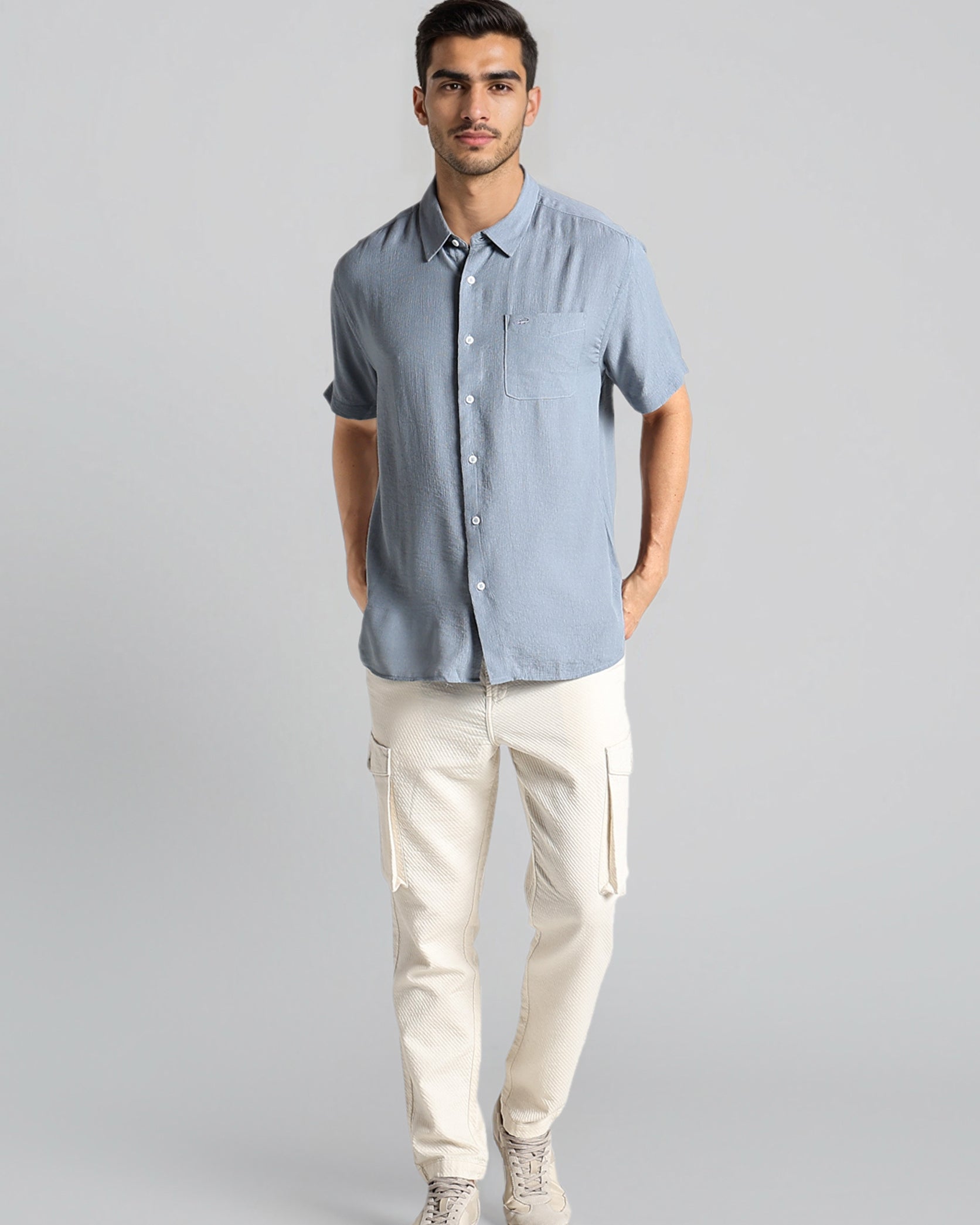 Man wearing a light blue button-up shirt and beige pants on a gray background