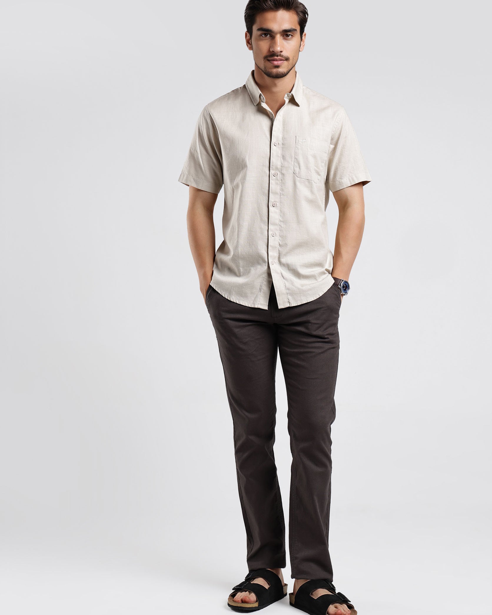 Man wearing a beige shirt and dark pants on a white background