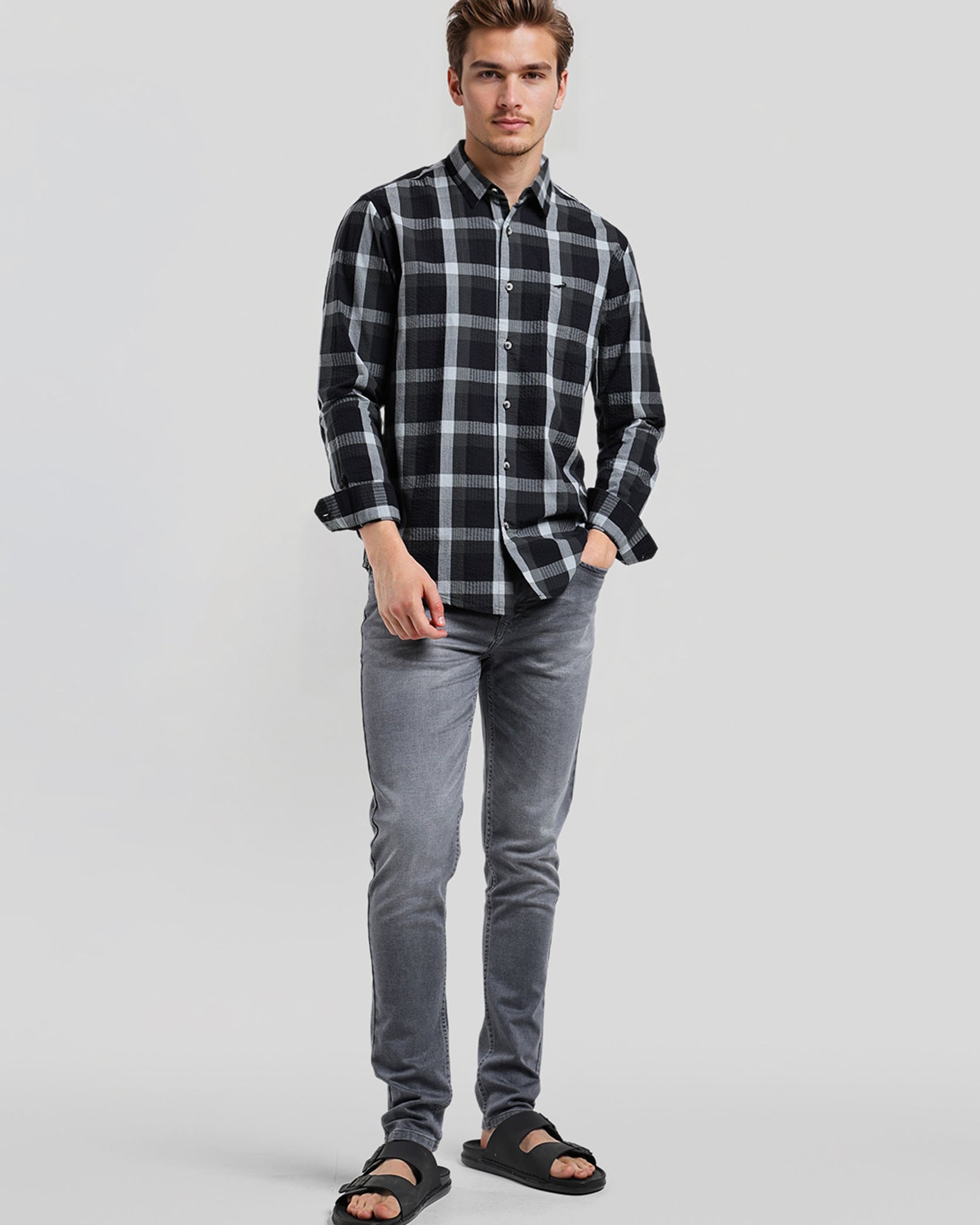 Man wearing a black and gray plaid shirt with gray jeans on a light gray background