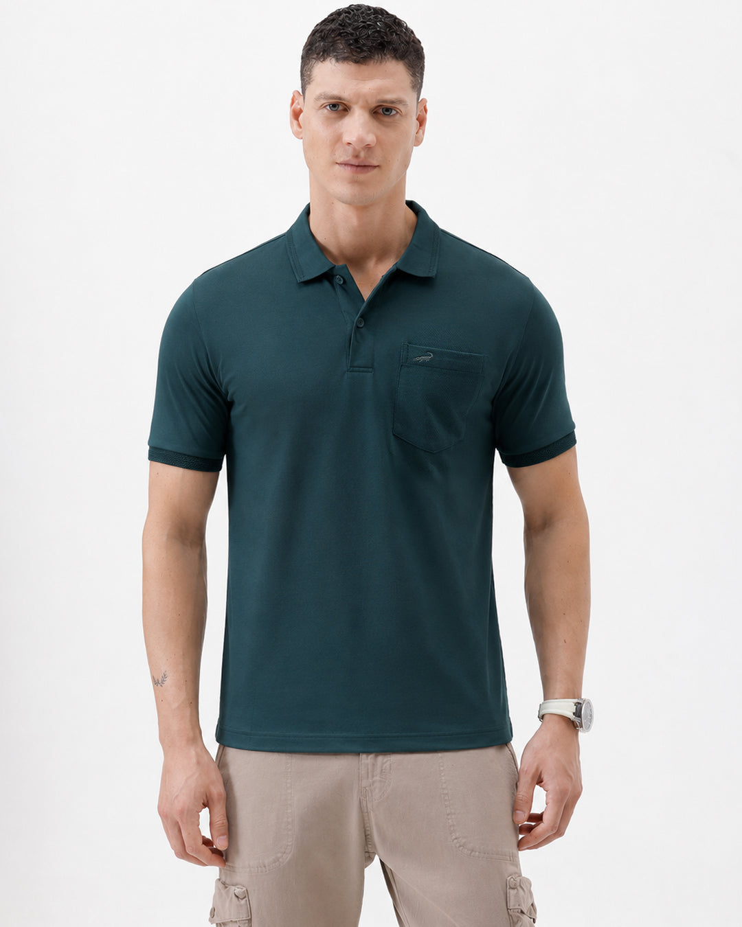 A man wearing a dark teal short-sleeve polo shirt with a chest pocket, paired with beige cargo pants, standing against a plain white studio background.