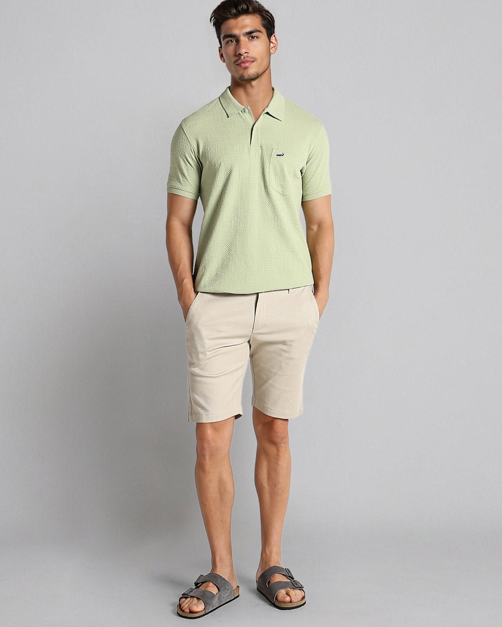 Man wearing a light green polo shirt and beige shorts on a gray background