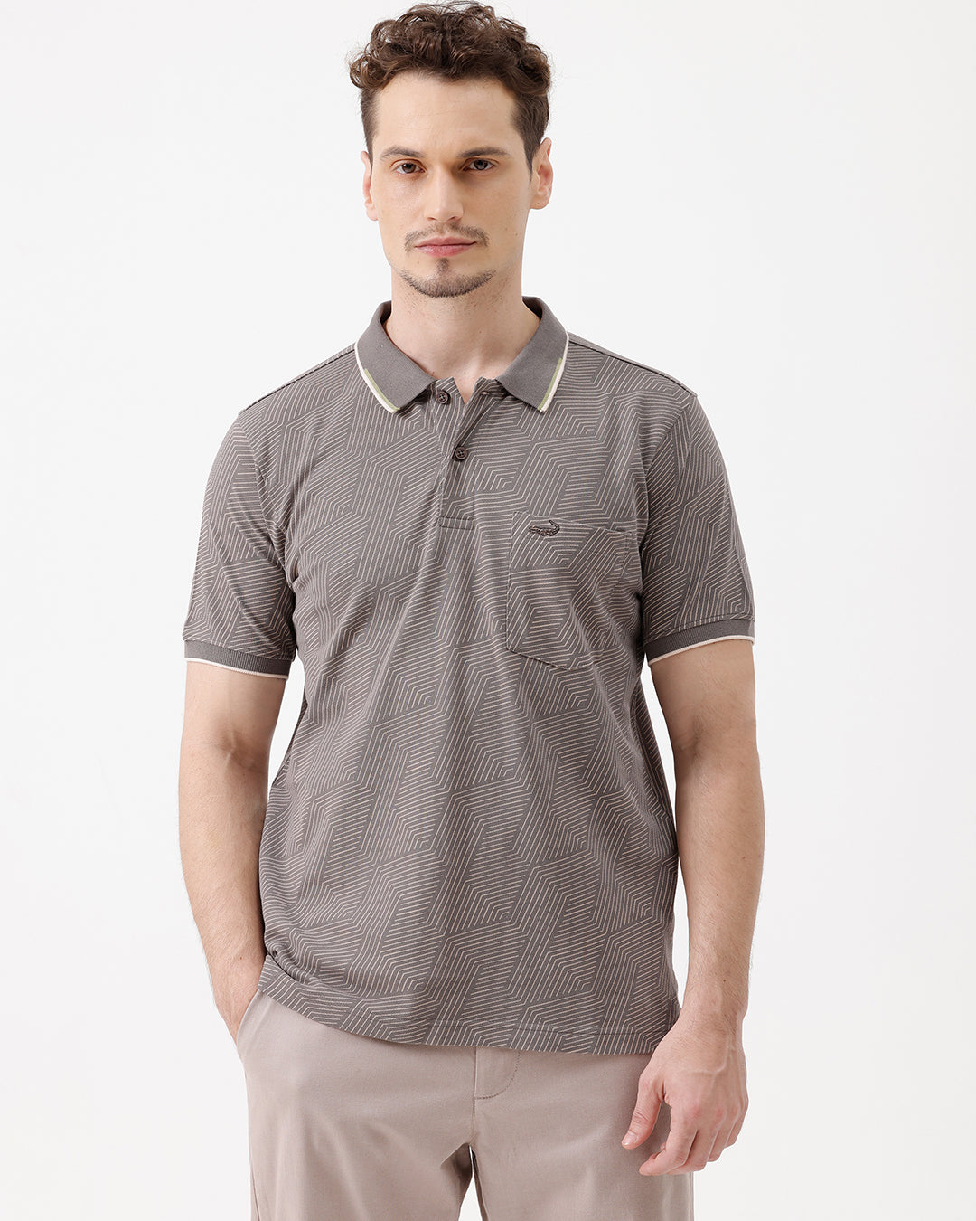 A man wearing a short-sleeve polo shirt with a gray and white geometric pattern, paired with beige trousers, standing against a plain white studio background.