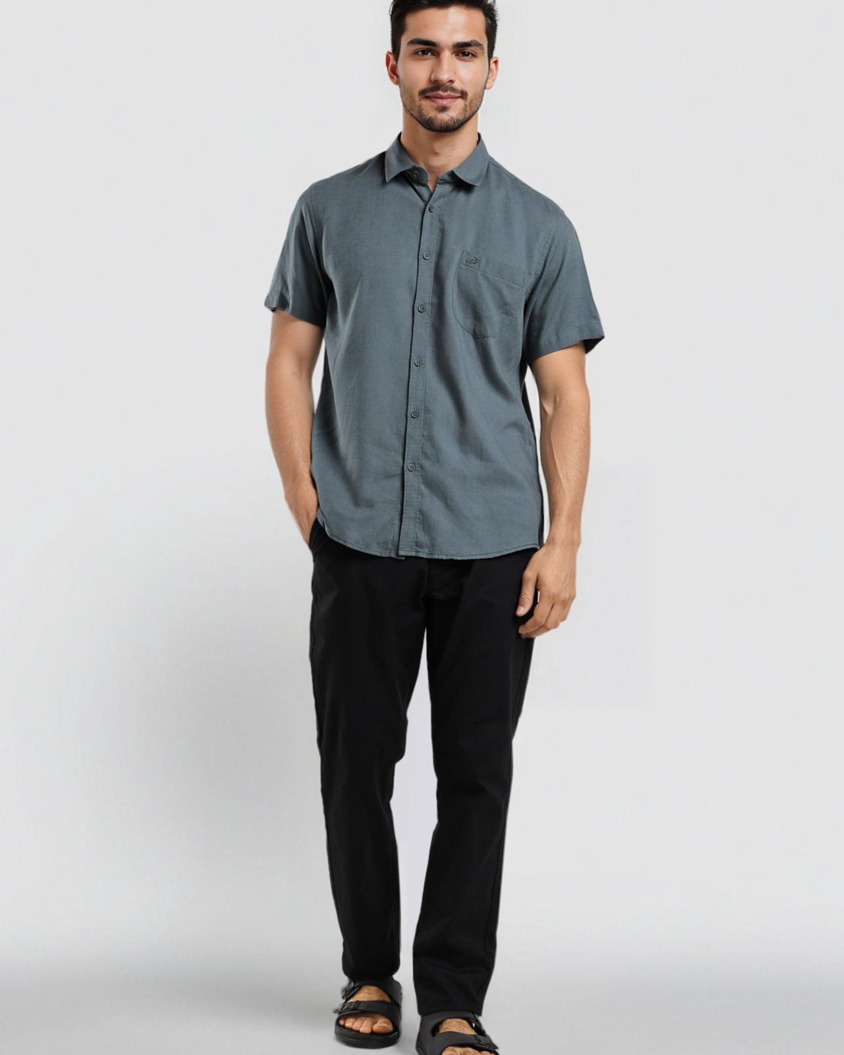 Man wearing a gray button-up shirt and black pants on a white background