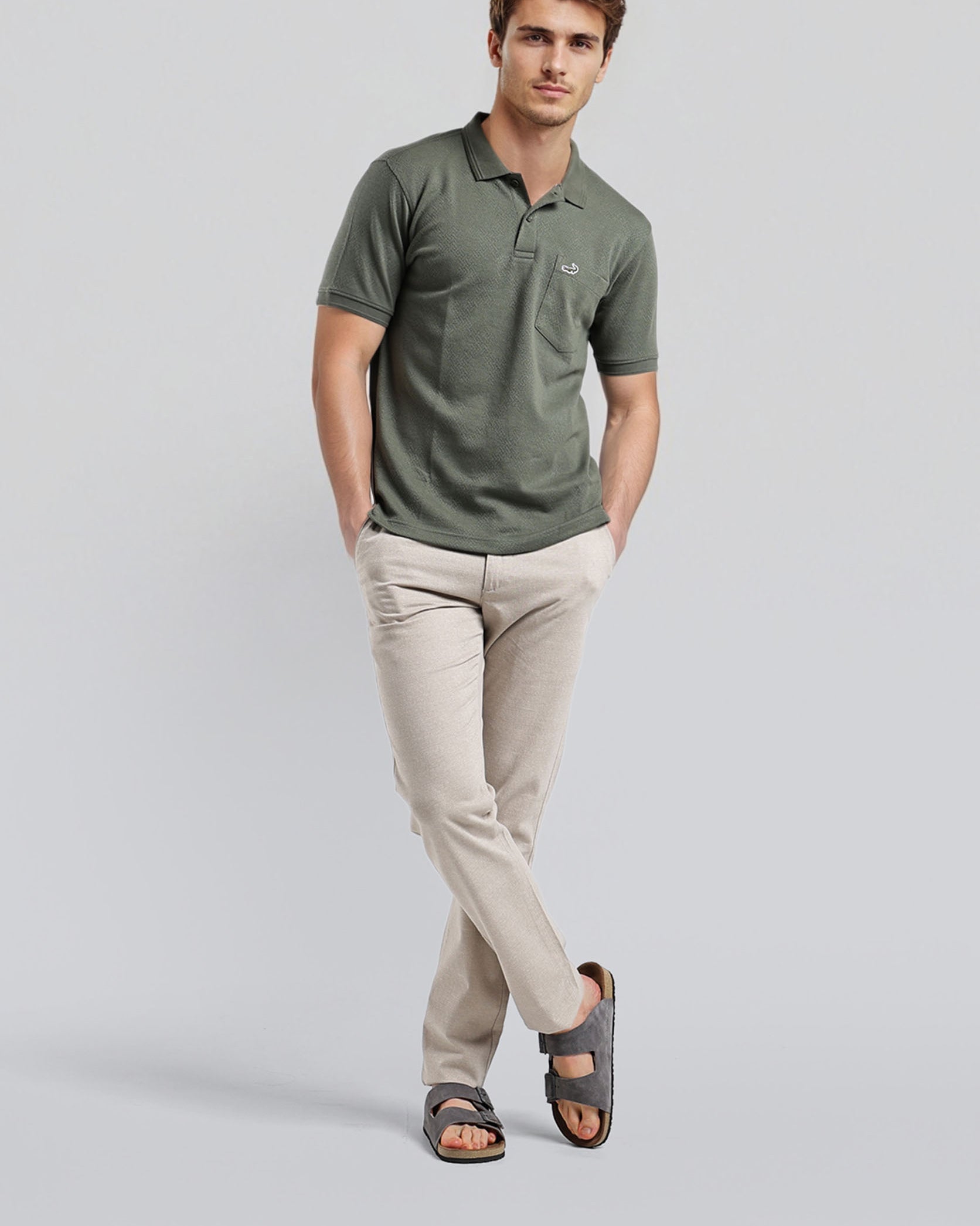 Man wearing a green polo shirt and beige pants on a light gray background
