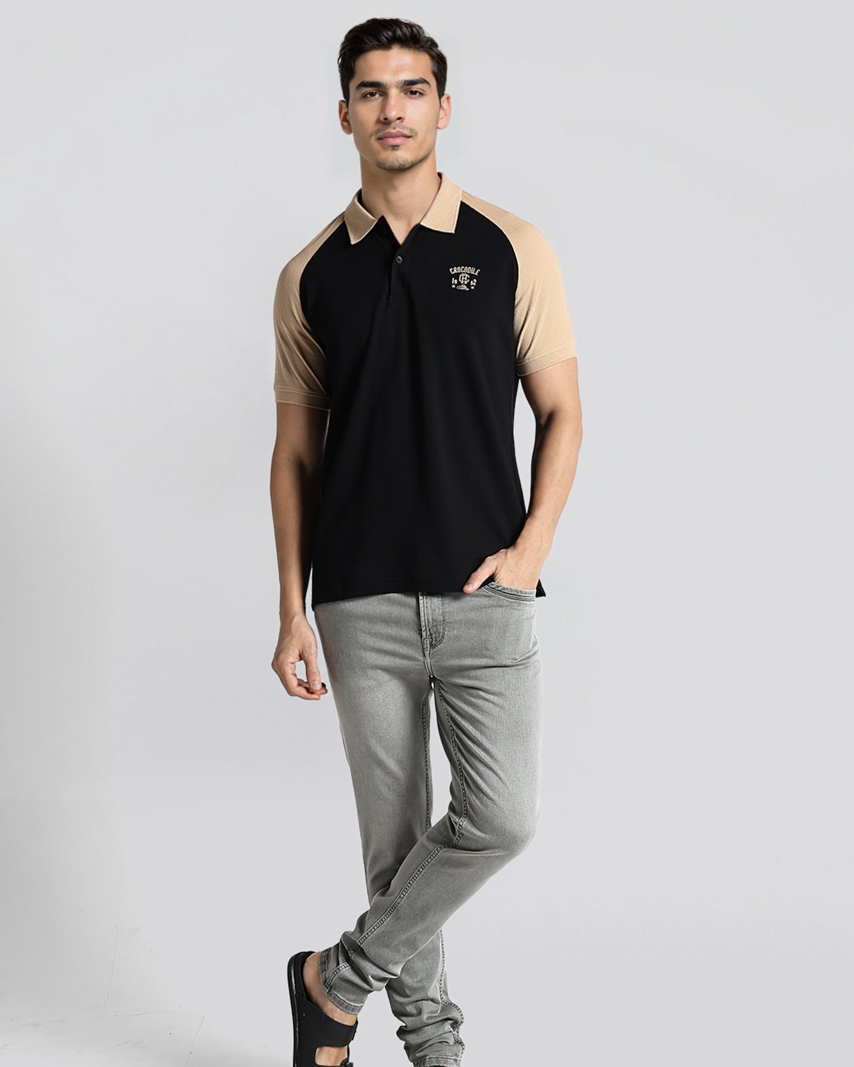 Man wearing a black and beige polo shirt with gray jeans on a white background