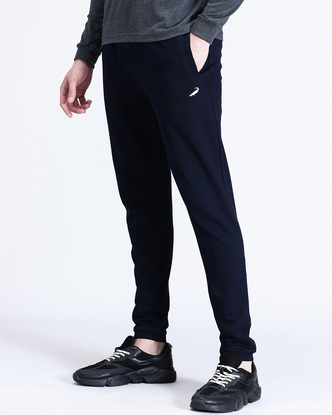 A person standing wearing solid navy comfort fit joggers with a grey top, paired with black sneakers.