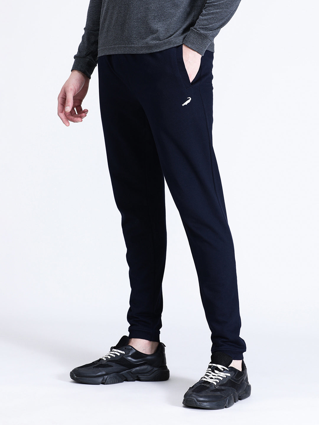 A person standing wearing solid navy comfort fit joggers with a grey top, paired with black sneakers.