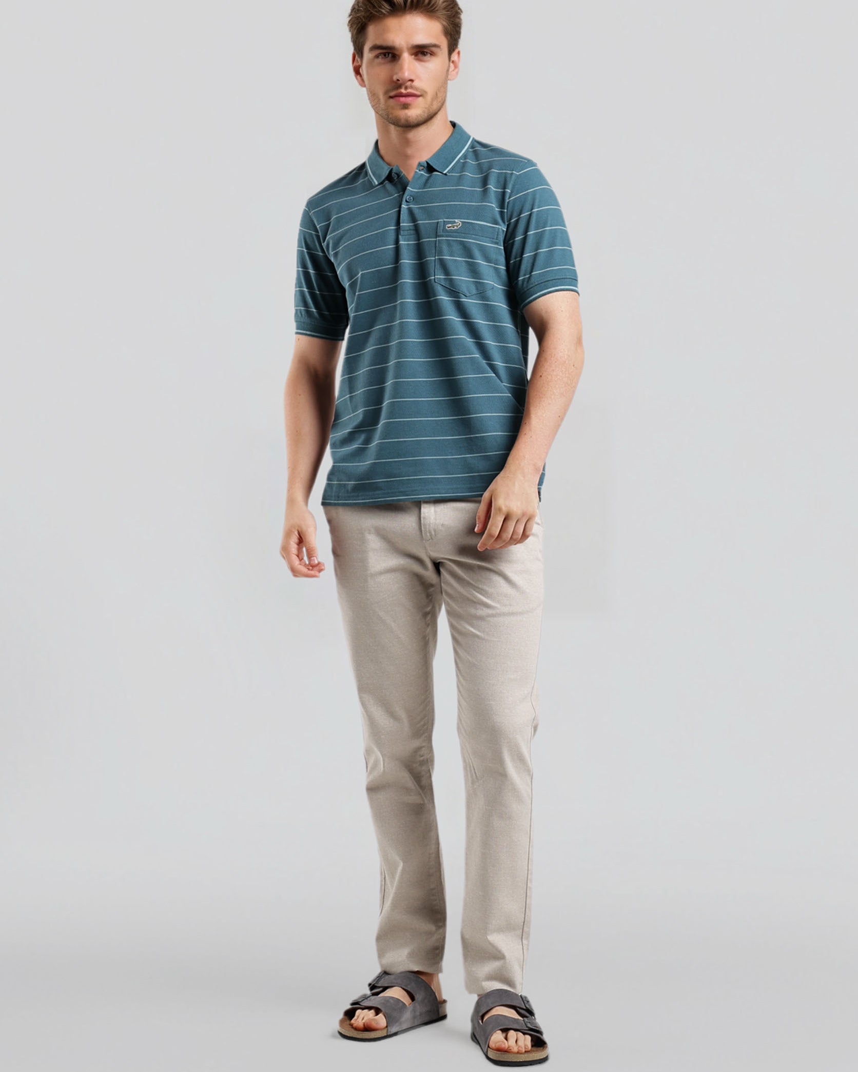 Man wearing a blue striped polo shirt and beige pants on a light gray background