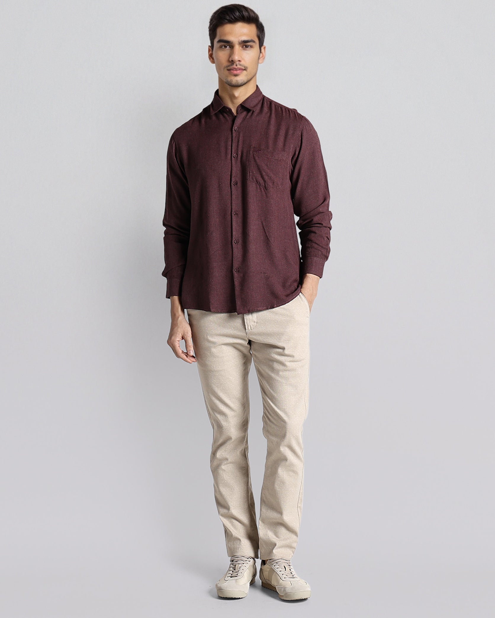 Man wearing a maroon shirt and beige pants on a light gray background