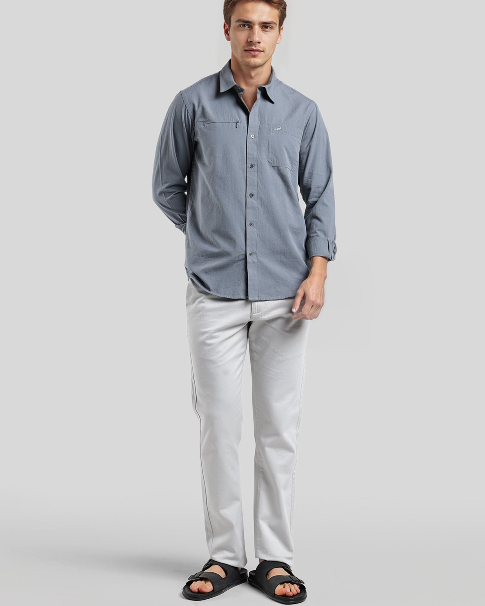 Man wearing a blue button-up shirt and light gray pants on a white background