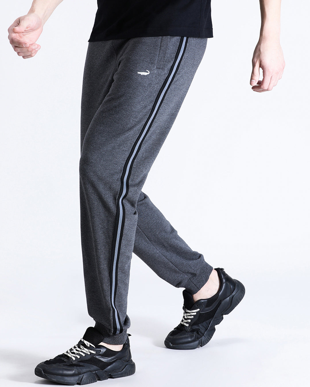 A person wearing charcoal grey classic fit joggers and black sneakers, standing on one leg to show the side view of the joggers.