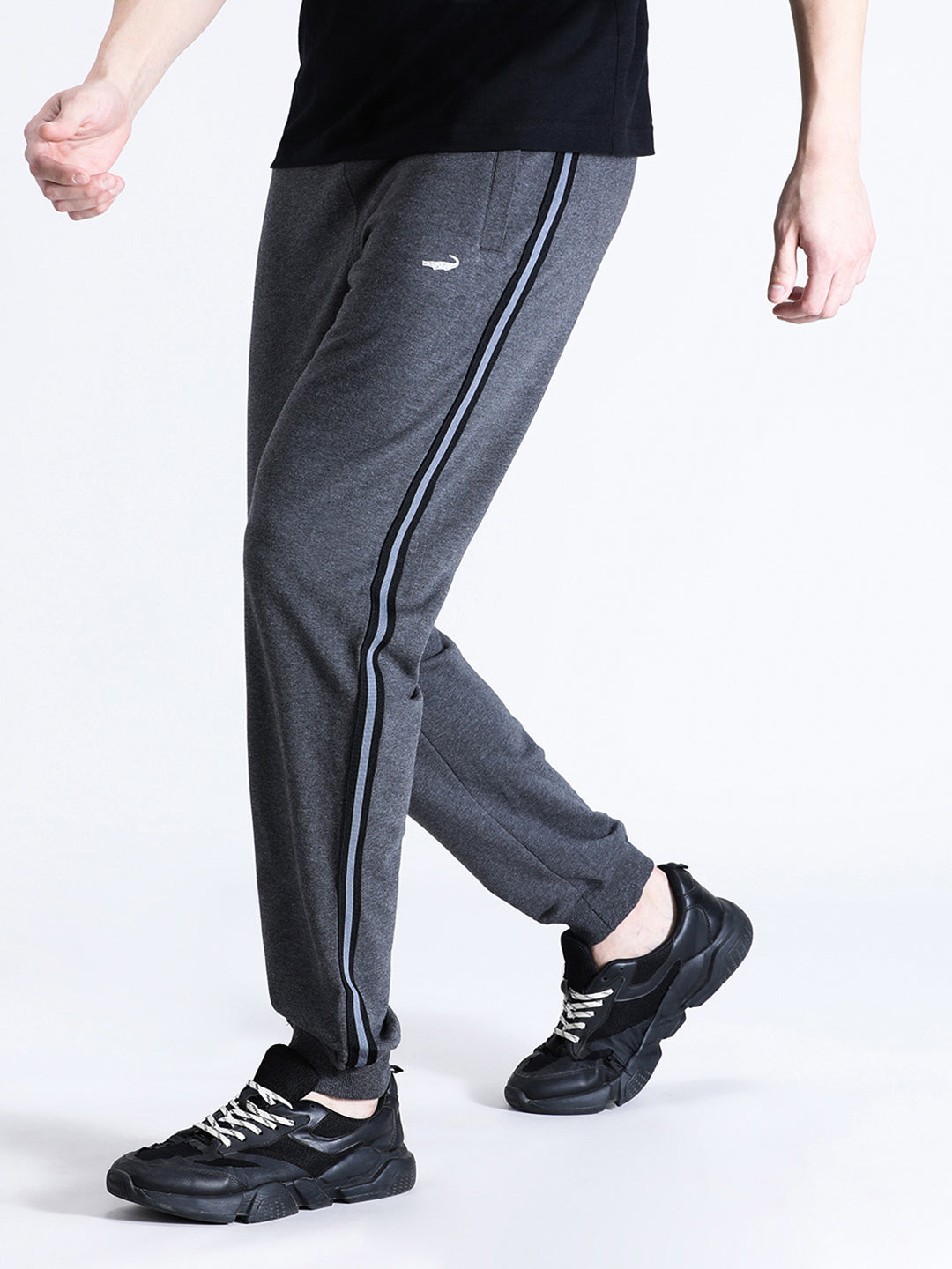 A person wearing charcoal grey classic fit joggers and black sneakers, standing on one leg to show the side view of the joggers.