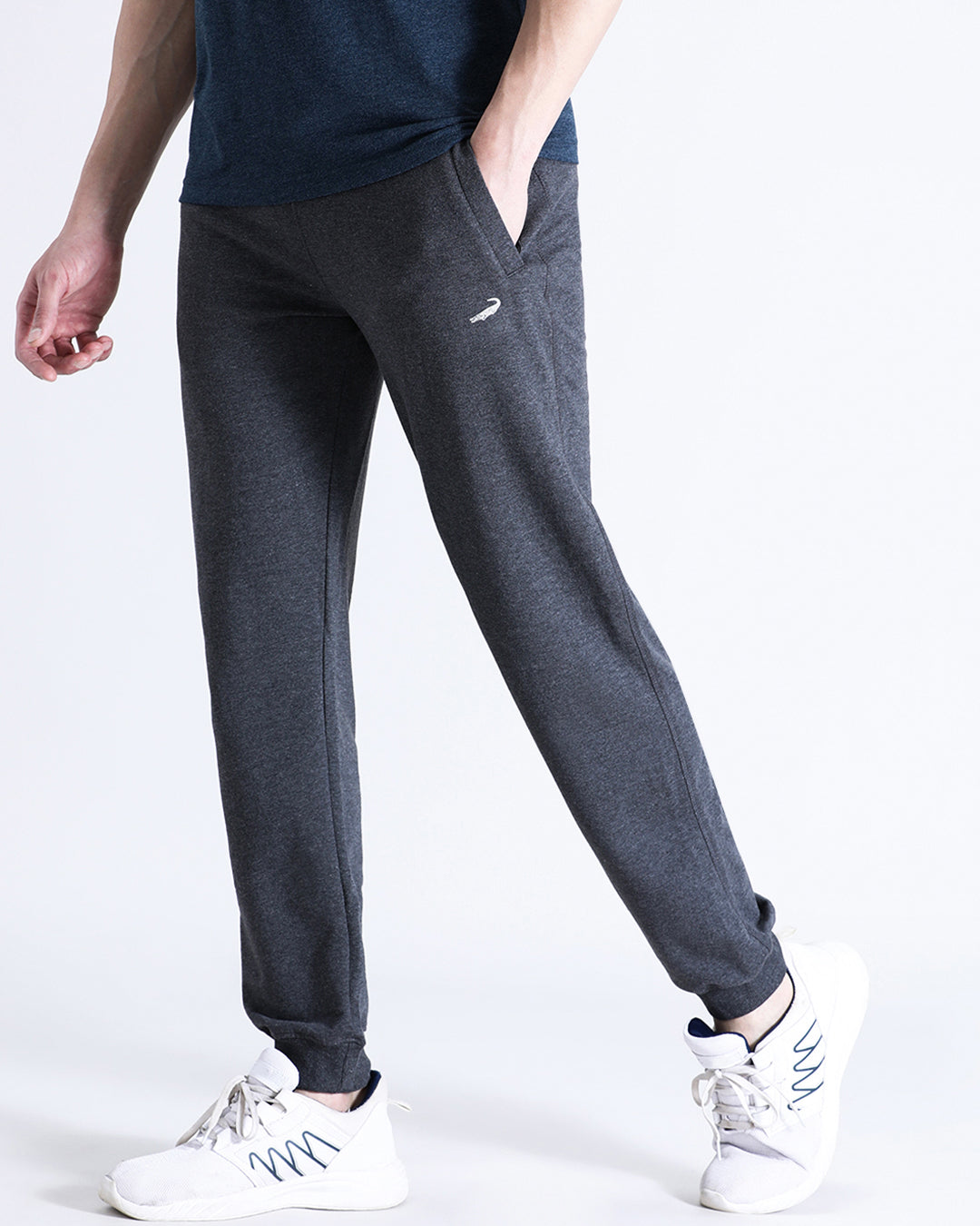 A person standing wearing charcoal grey classic fit joggers with a solid pattern, paired with a blue top and white sneakers.