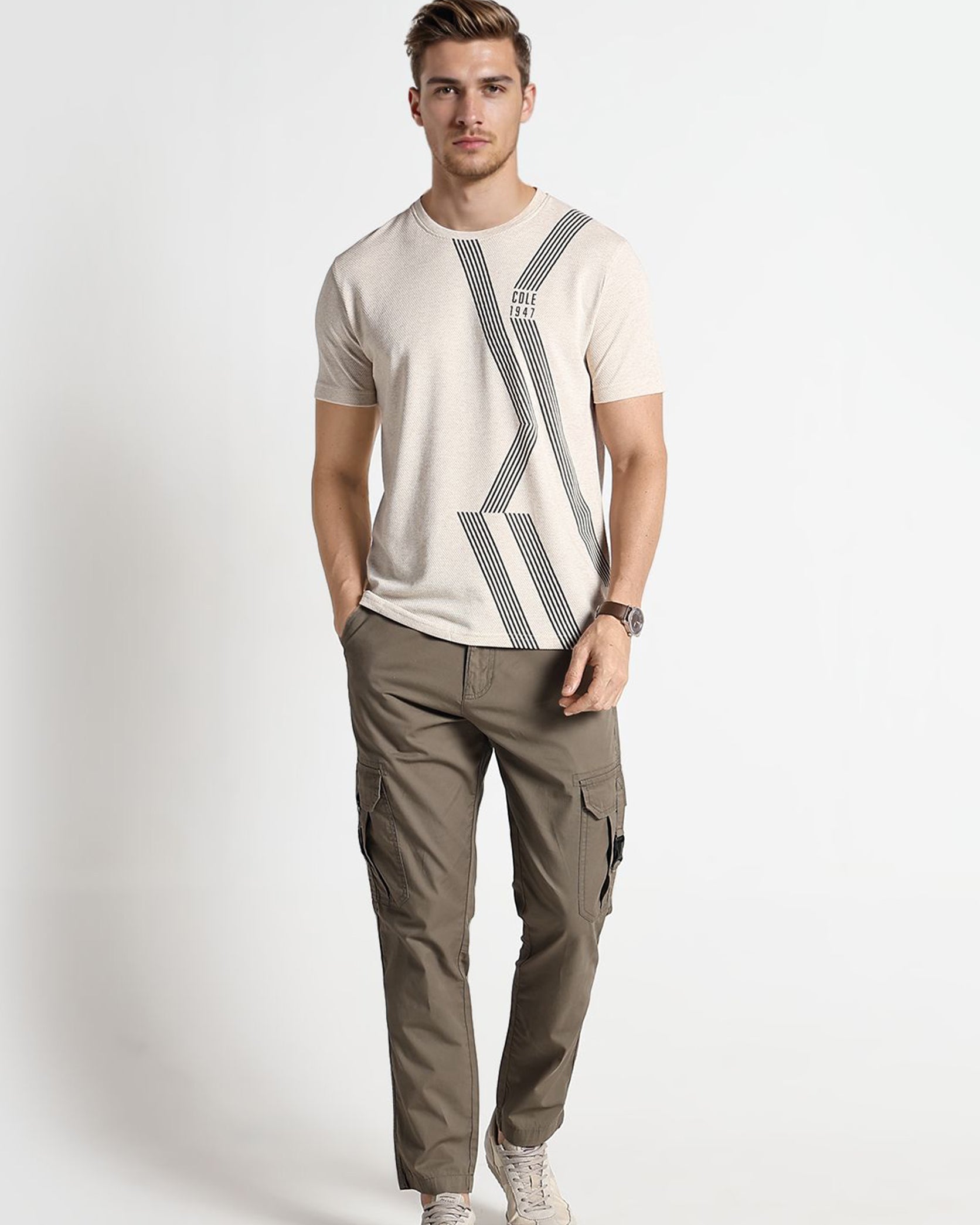 Man wearing a beige t-shirt with a geometric design and green cargo pants on a white background