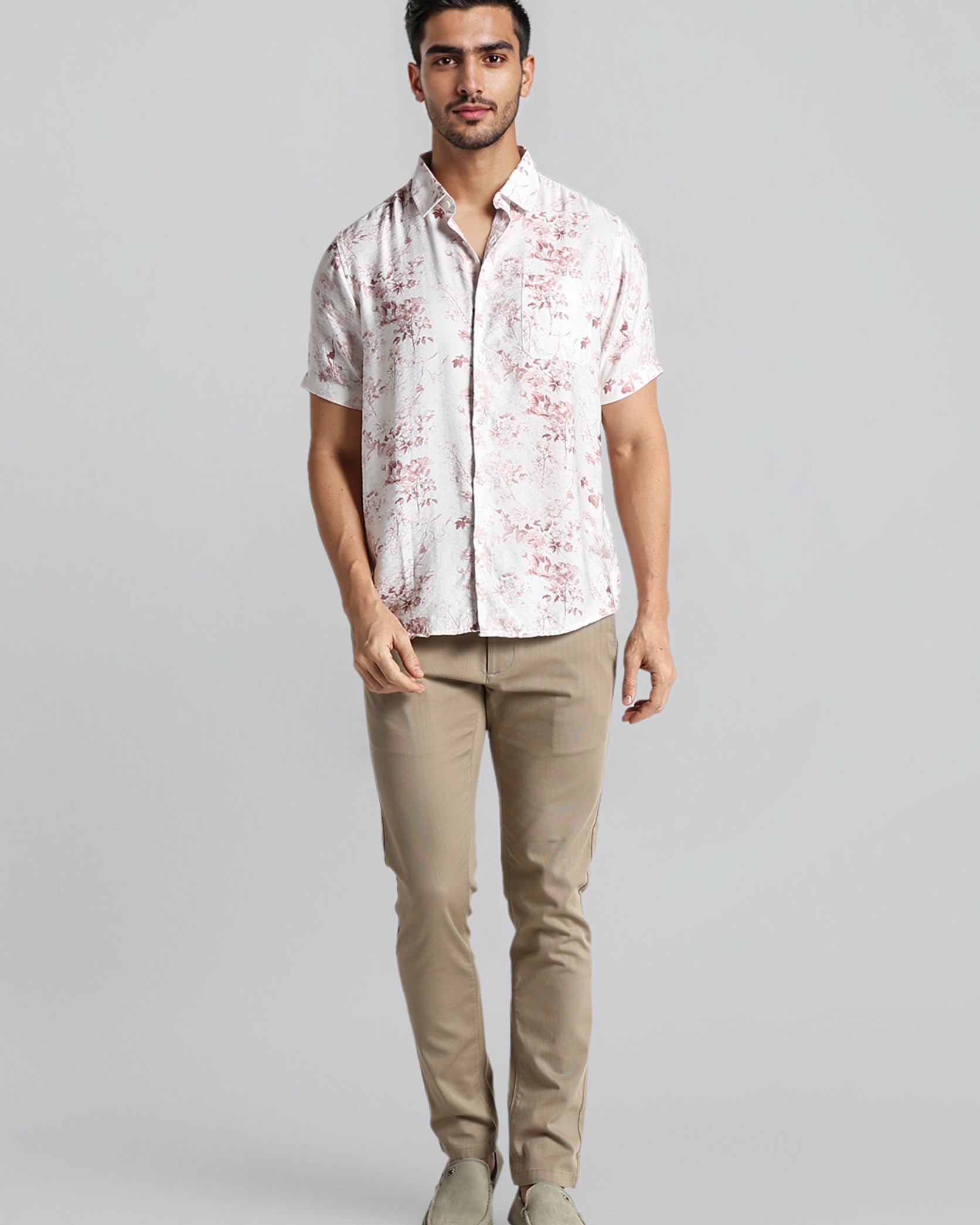 Man wearing a patterned shirt and beige pants on a gray background