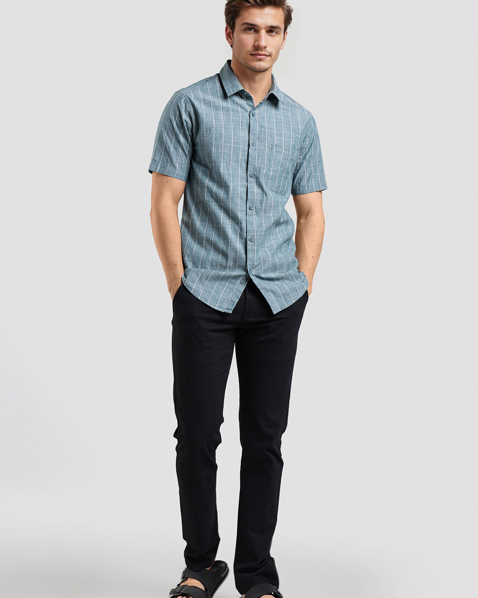 Man wearing a blue checkered shirt and black pants on a white background