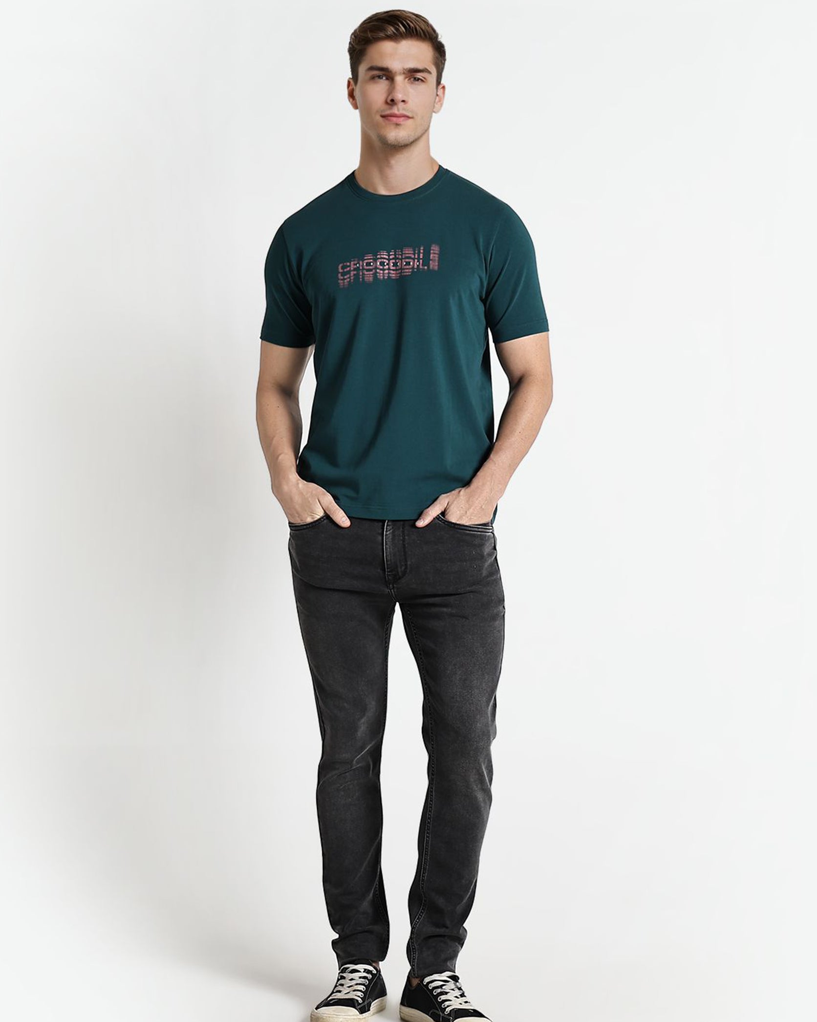 Man wearing a green t-shirt with text and dark jeans on a white background