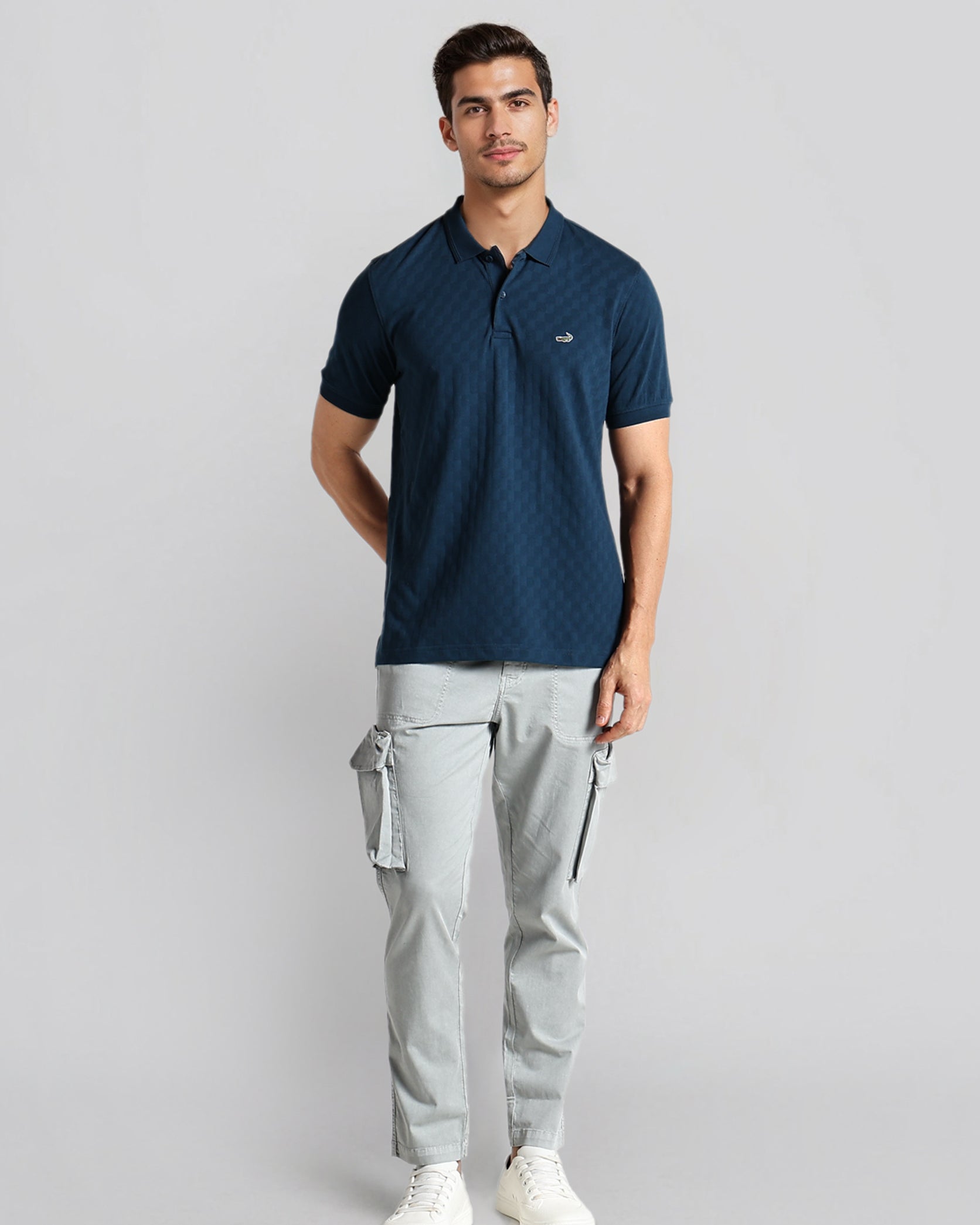 Man wearing a navy polo shirt and gray cargo pants on a light gray background