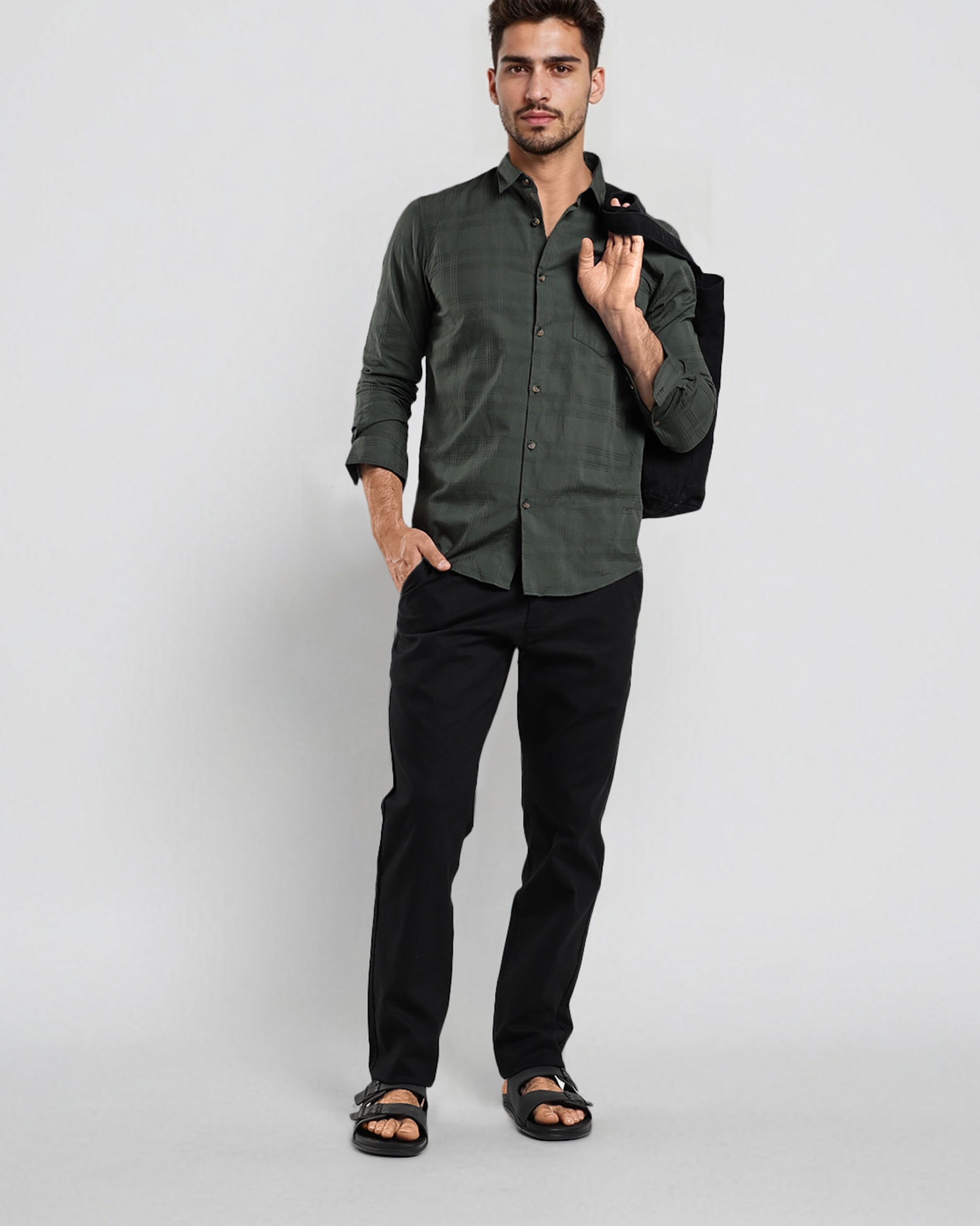 Man wearing a green shirt and black pants holding a black jacket against a white background