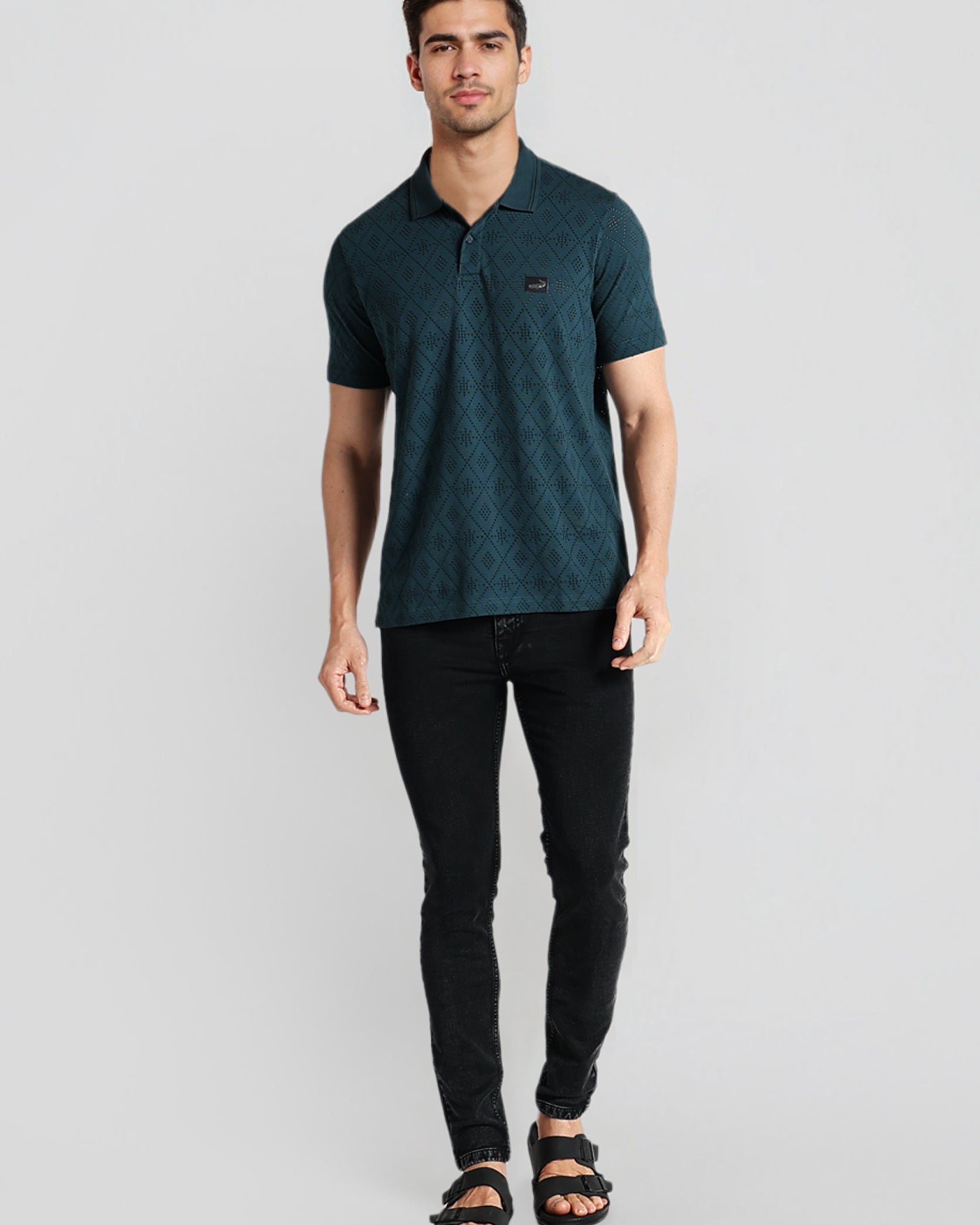 Man wearing a dark green polo shirt and black pants on a light gray background