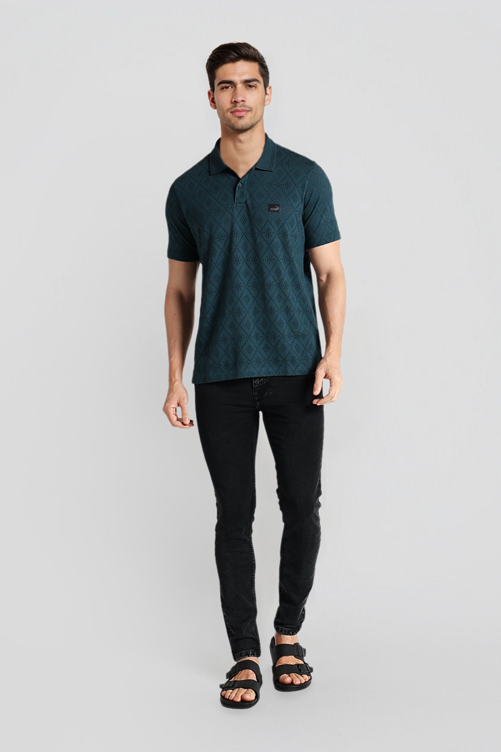 Man wearing a dark green polo shirt and black pants on a light gray background