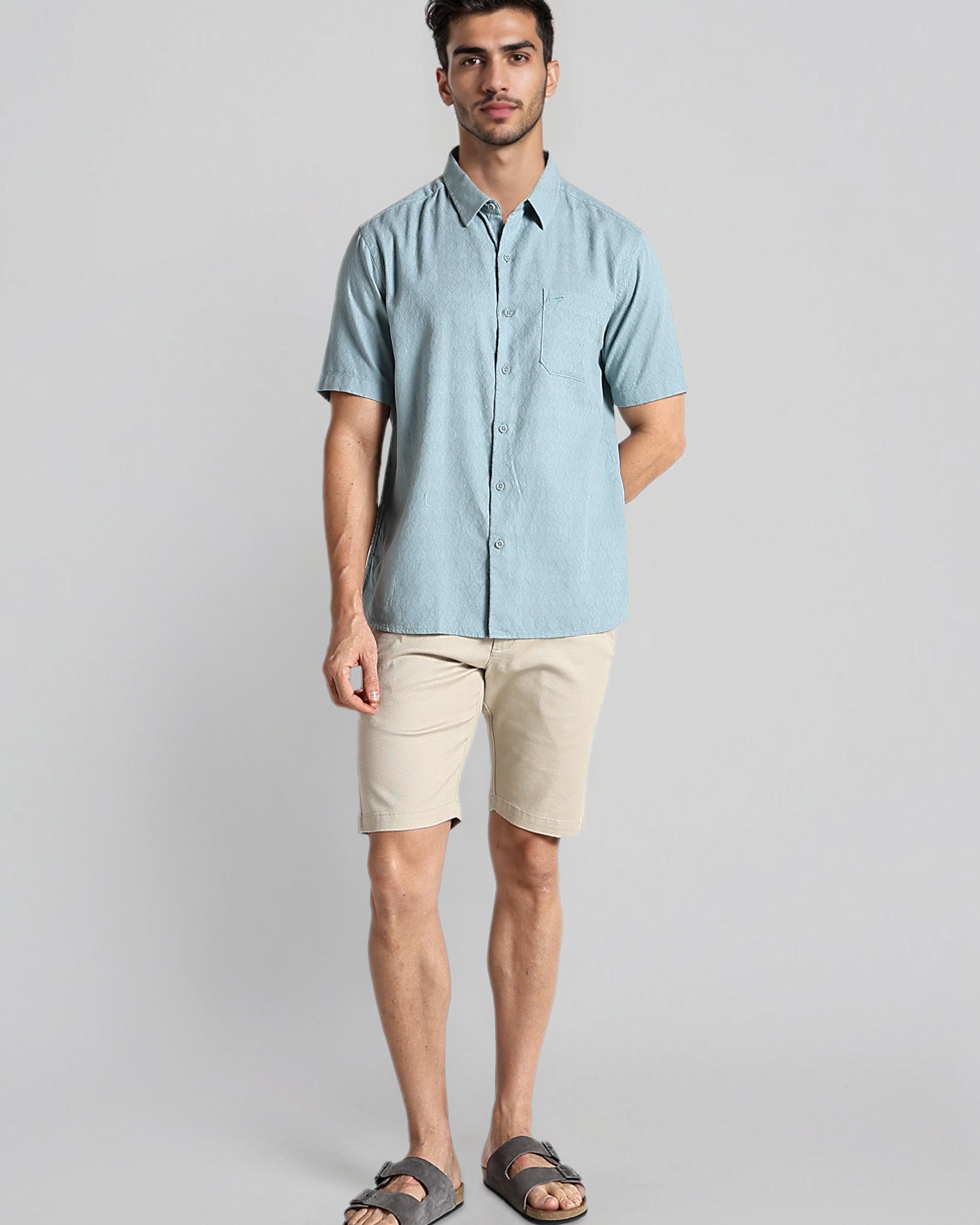 Man wearing a light blue shirt and beige shorts on a gray background