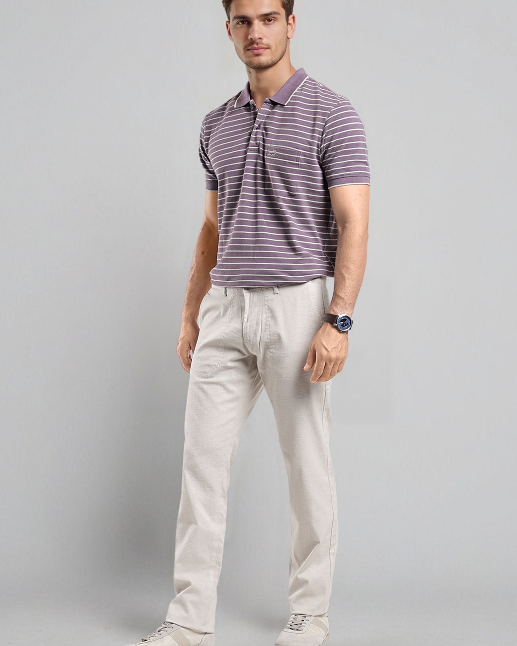 Man wearing a striped polo shirt and light-colored pants on a gray background