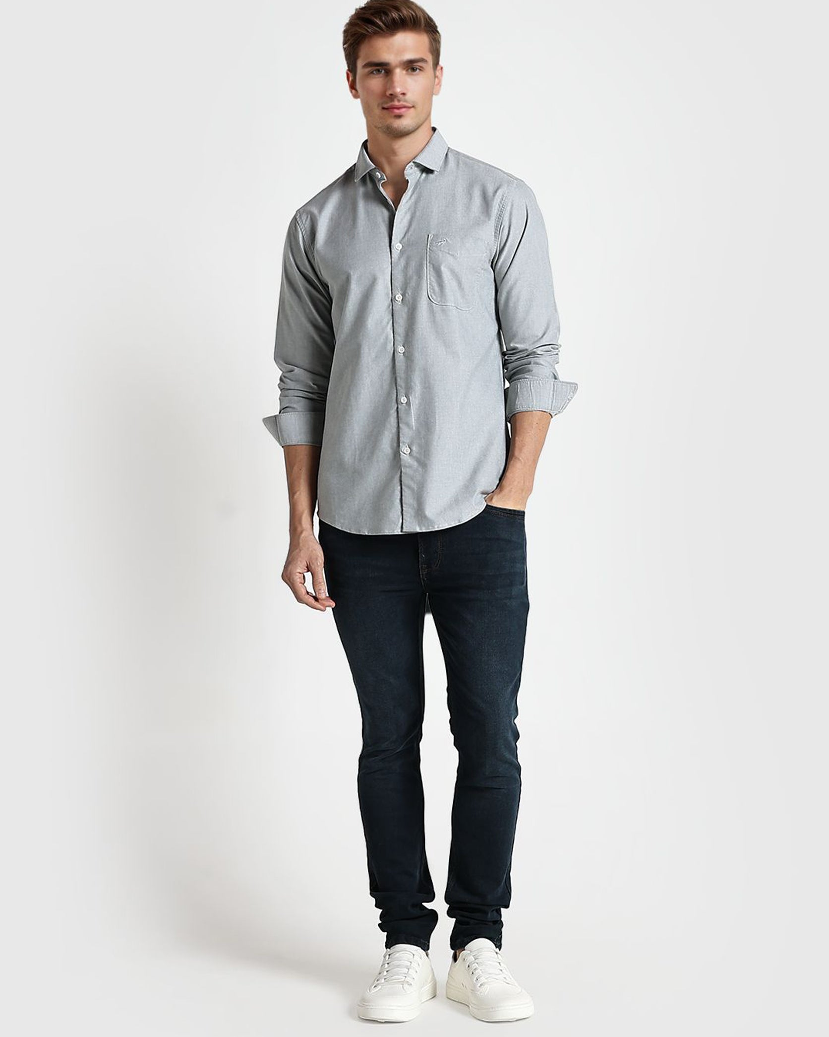 Man wearing a light gray button-up shirt and dark jeans on a white background
