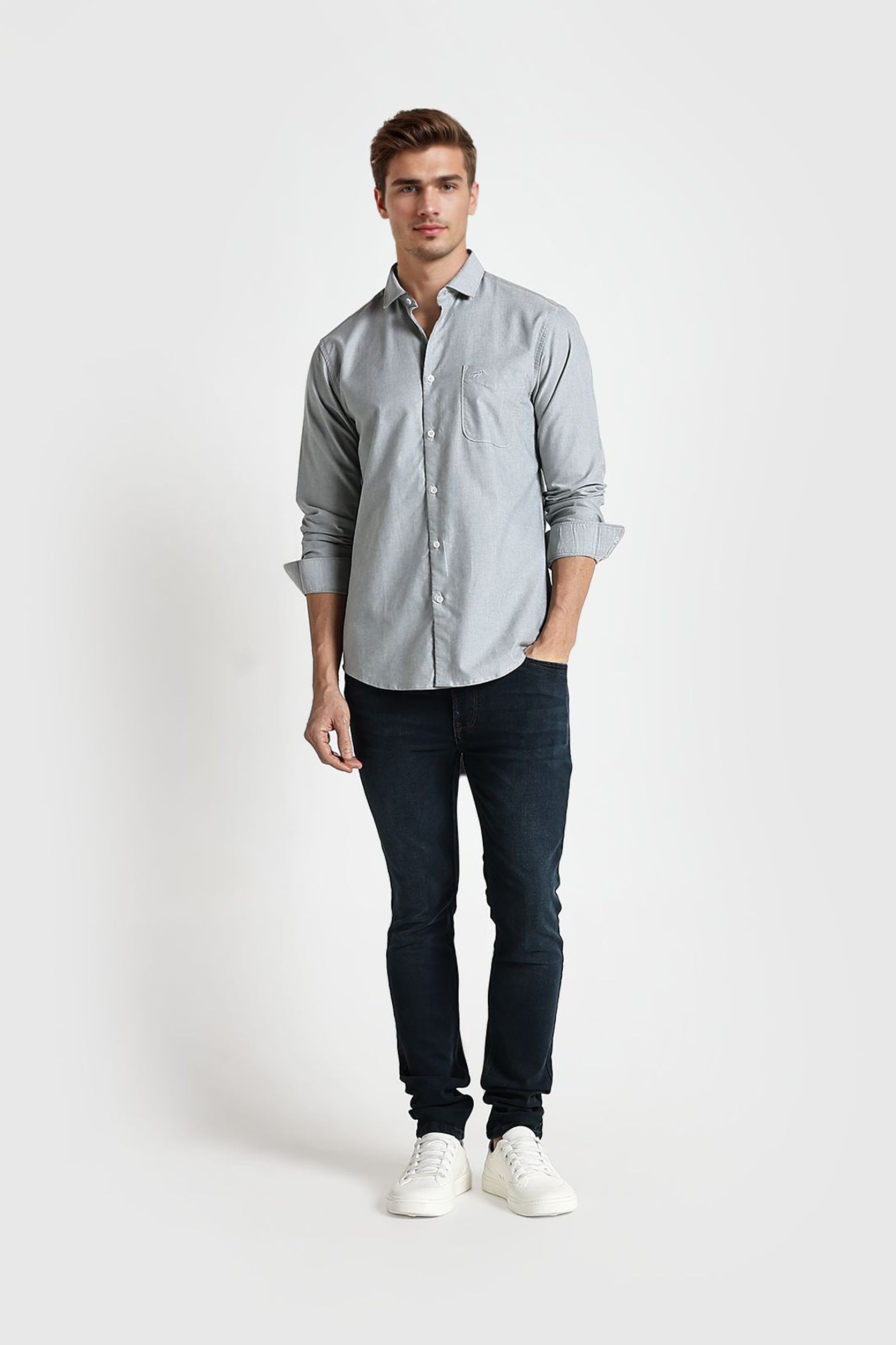 Man wearing a light gray button-up shirt and dark jeans on a white background