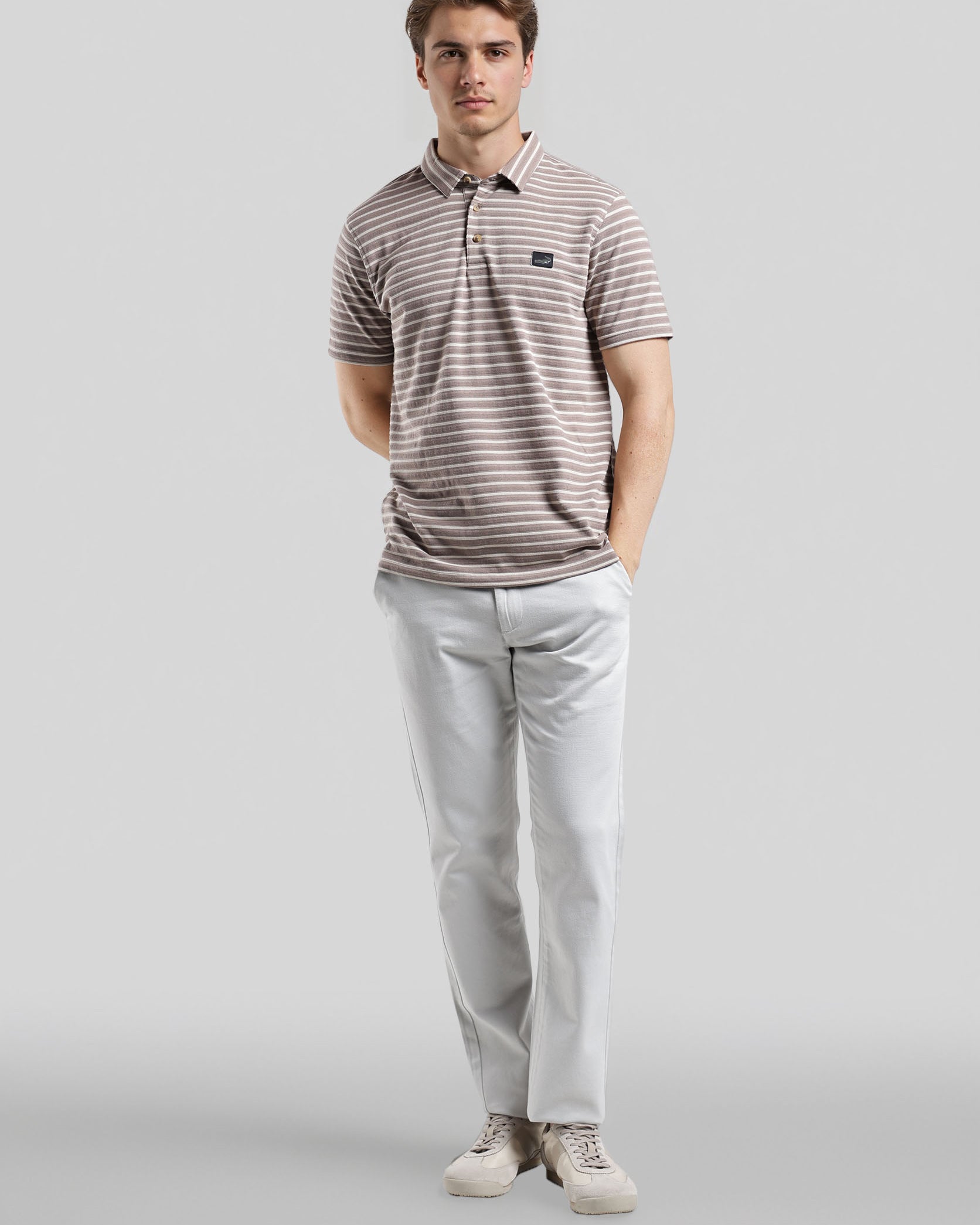 Man wearing a striped polo shirt and light-colored pants on a gray background