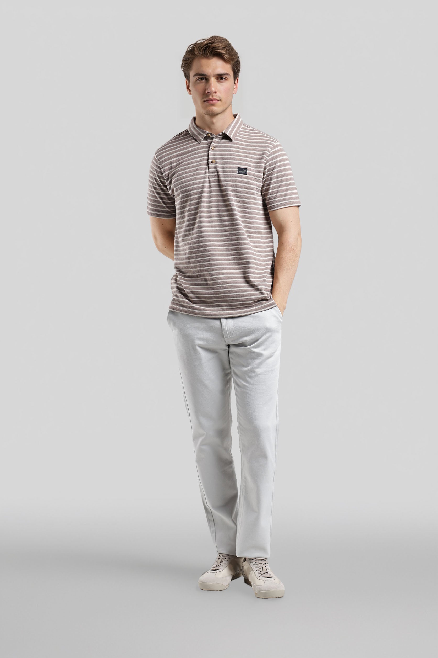 Man wearing a striped polo shirt and light-colored pants on a gray background