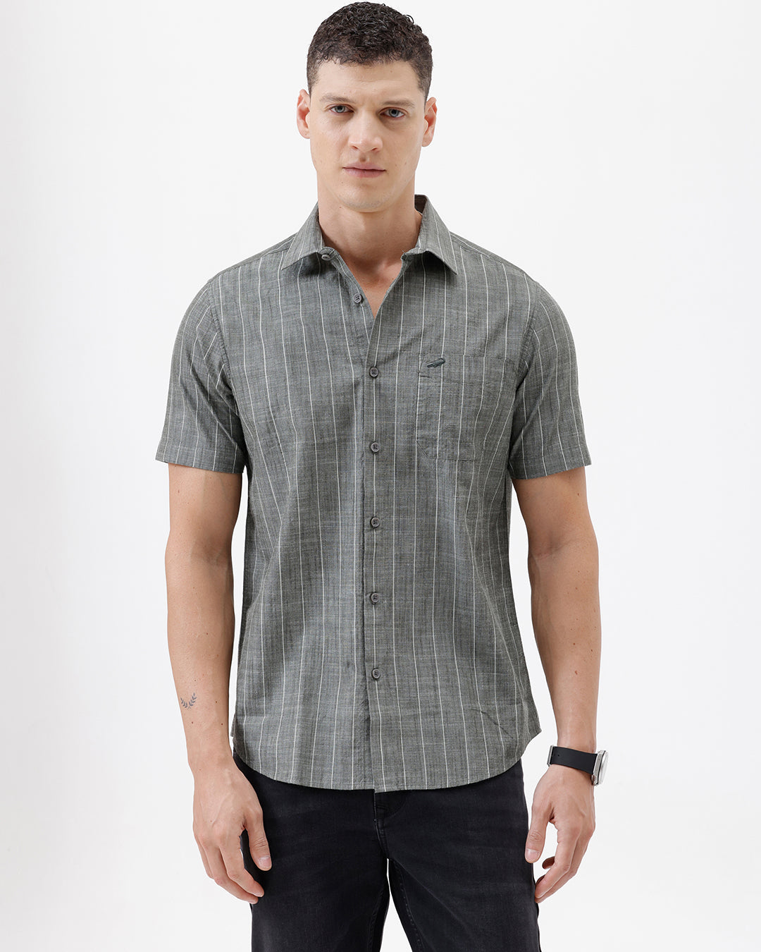 A man wearing a short-sleeve button-up shirt with a gray and white vertical stripe pattern, paired with black pants, standing against a plain white studio background.