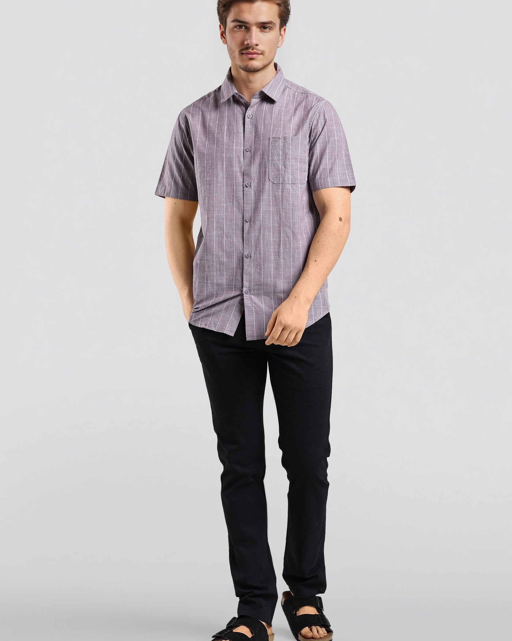 Man wearing a short-sleeve checkered shirt and black pants on a light gray background