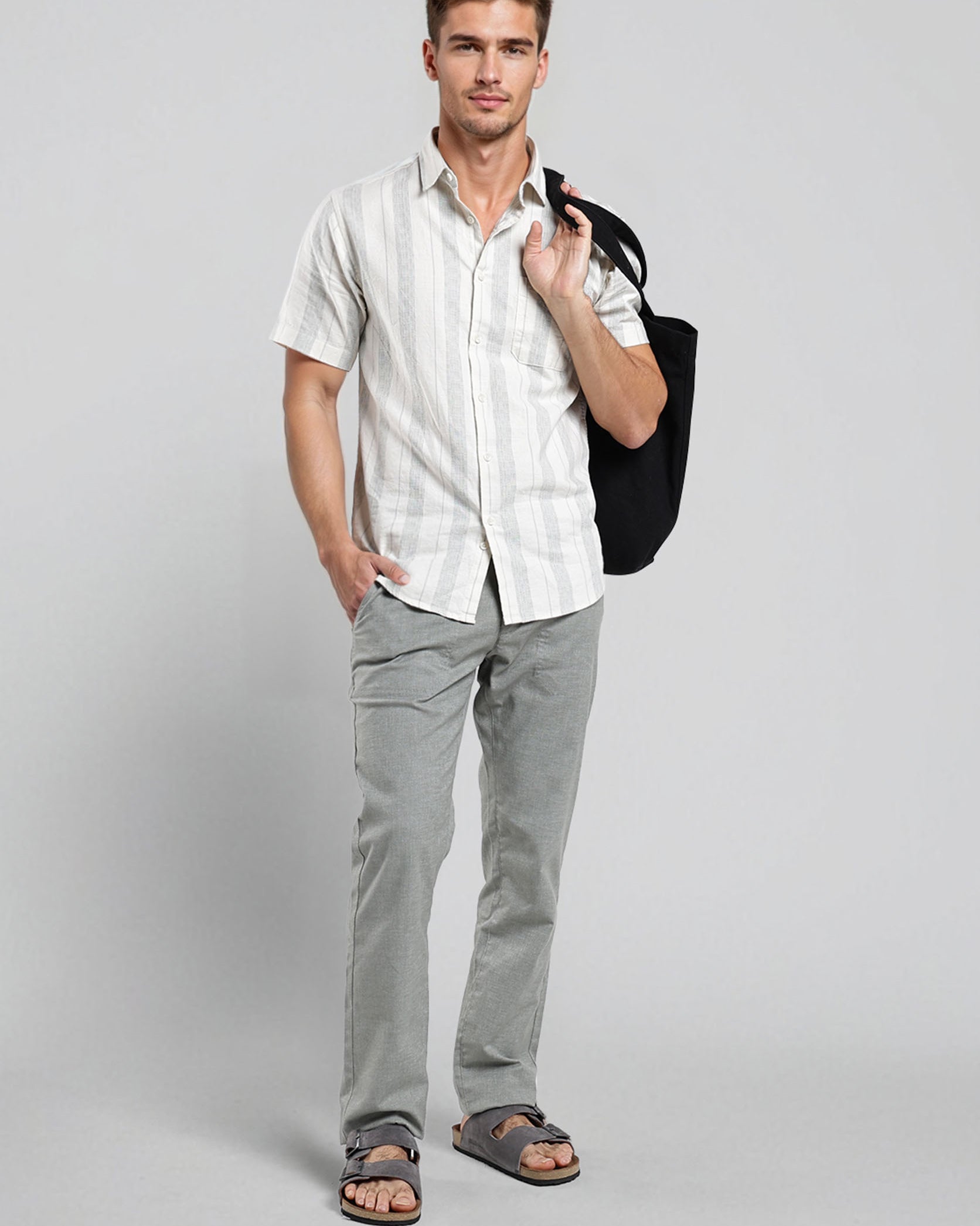 Man wearing a white shirt and gray pants holding a black bag on a gray background