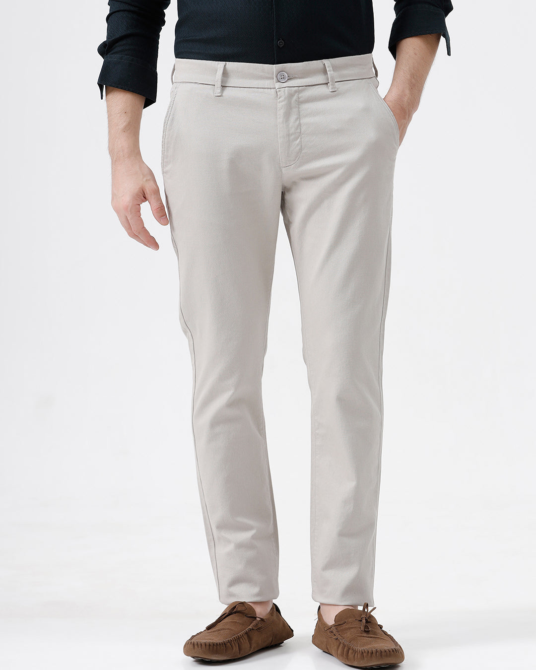 A person wearing slim-fit light beige chino pants, paired with a dark navy long-sleeve button-up shirt and brown suede moccasin-style shoes, photographed against a clean white studio background.