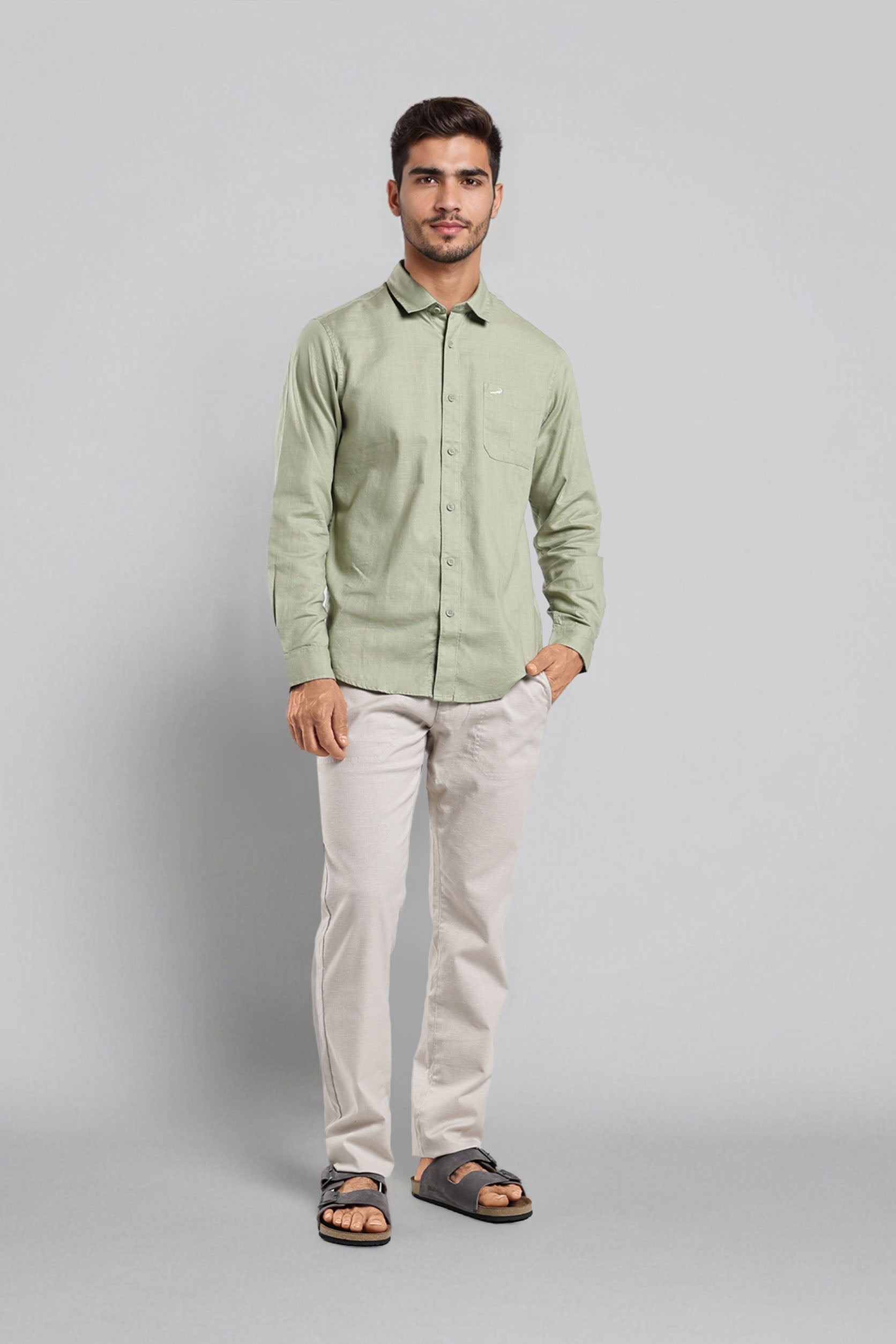 Man wearing a light green shirt and white pants on a gray background