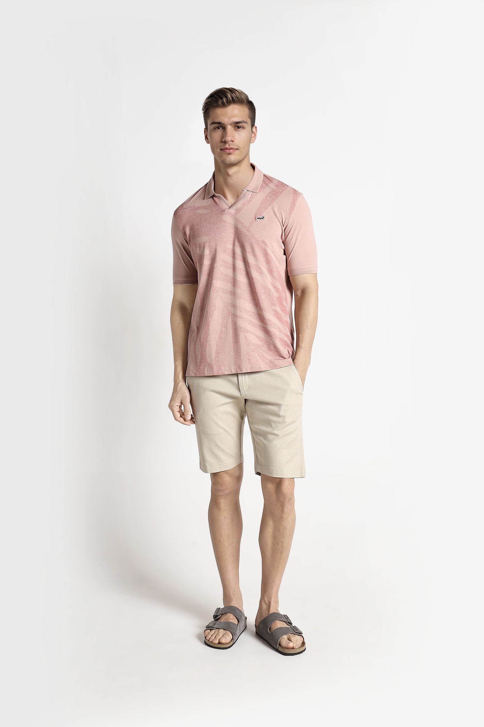 Man wearing a pink polo shirt and beige shorts on a white background