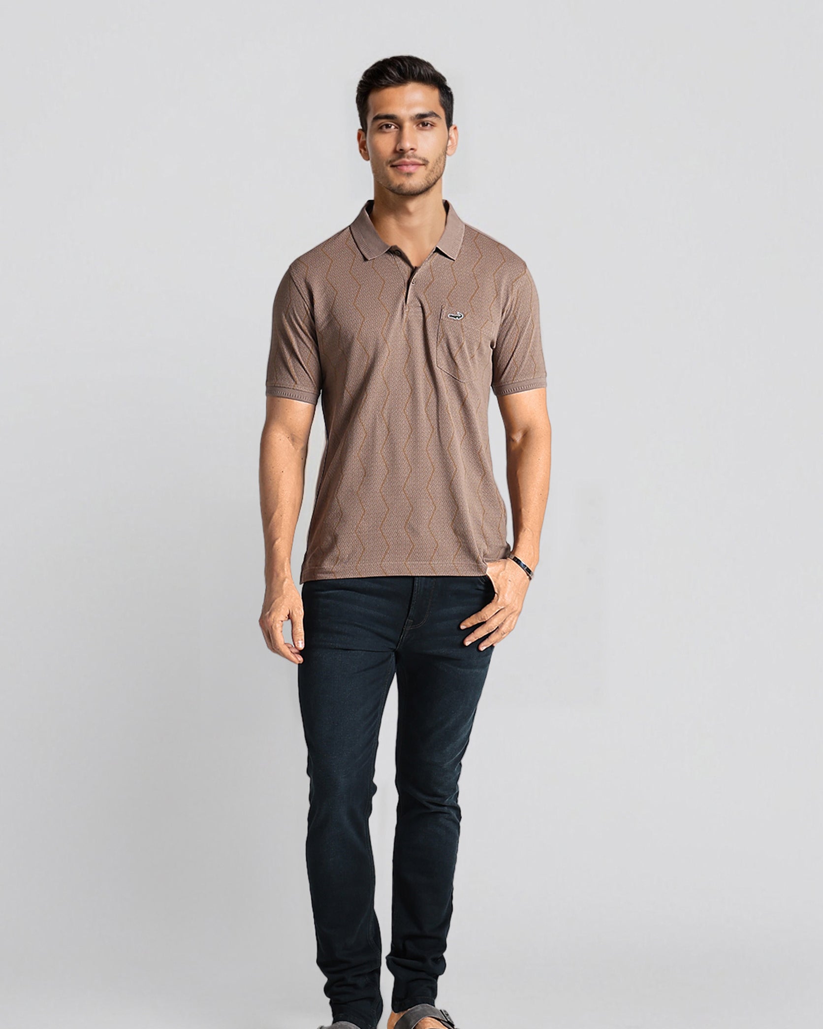 Man wearing a brown polo shirt and dark jeans on a light gray background