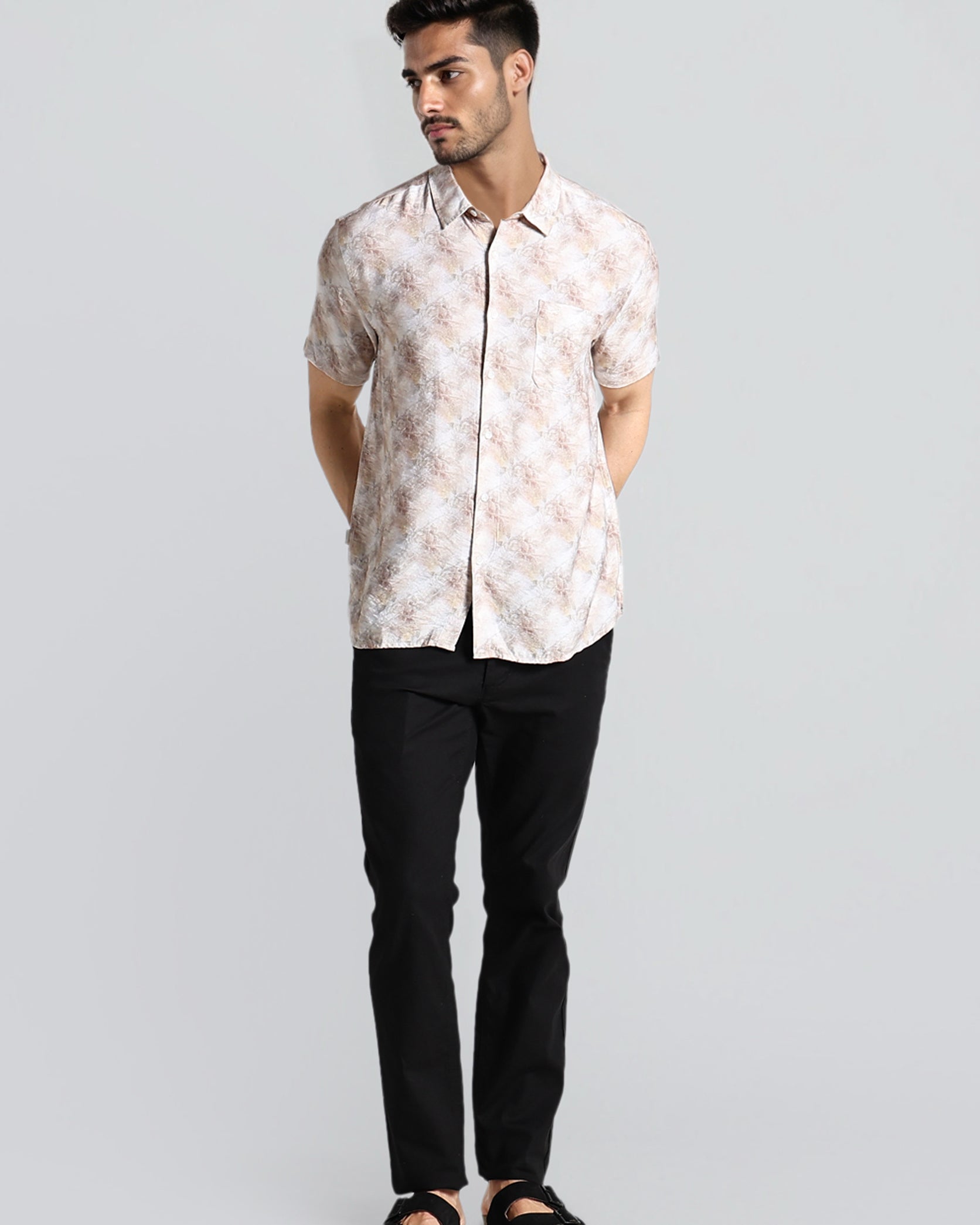 Man wearing a white floral shirt and black pants on a light gray background