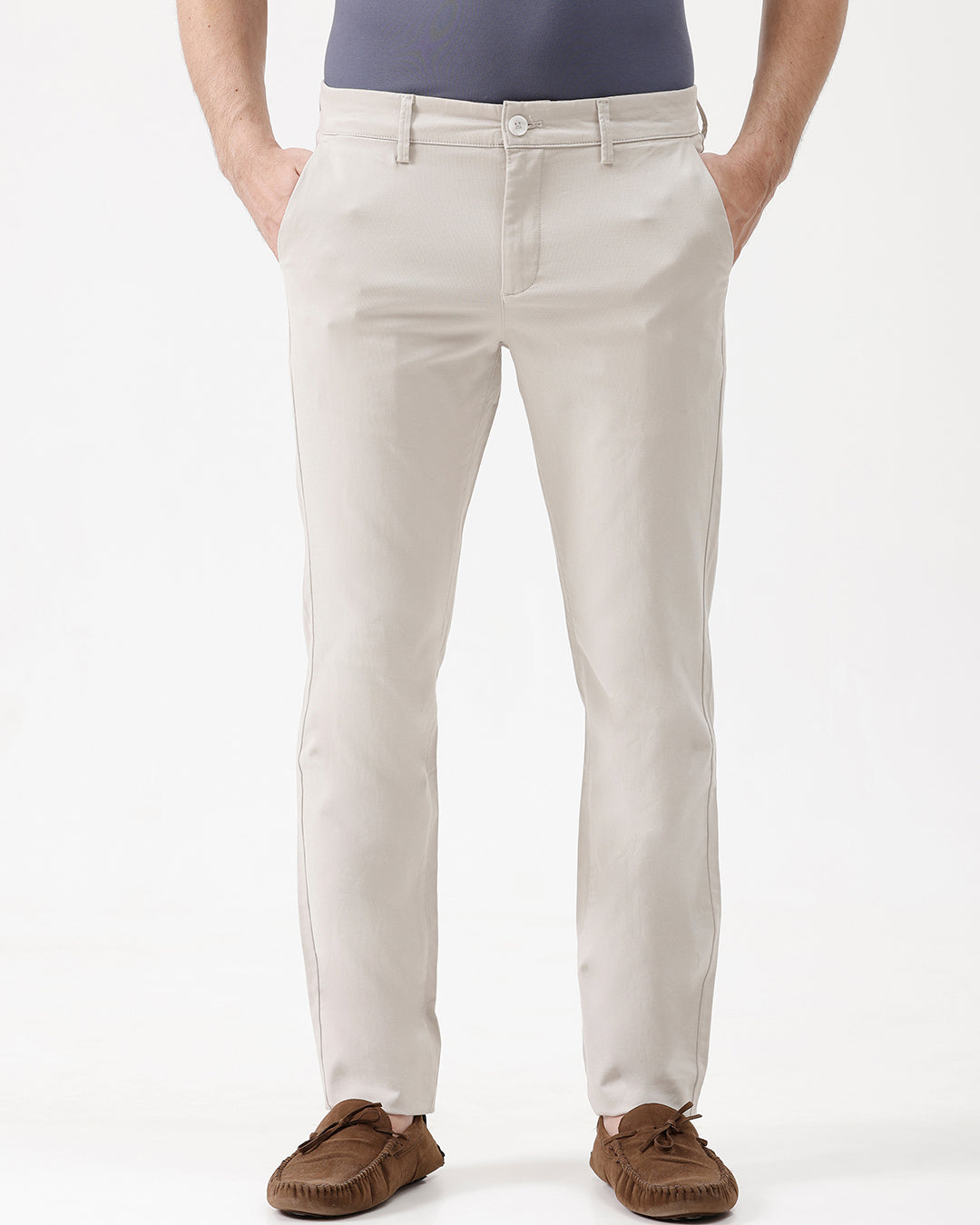 A person wearing light beige chino pants, a dark blue-gray t-shirt, and brown suede moccasin shoes, standing against a plain white studio background.