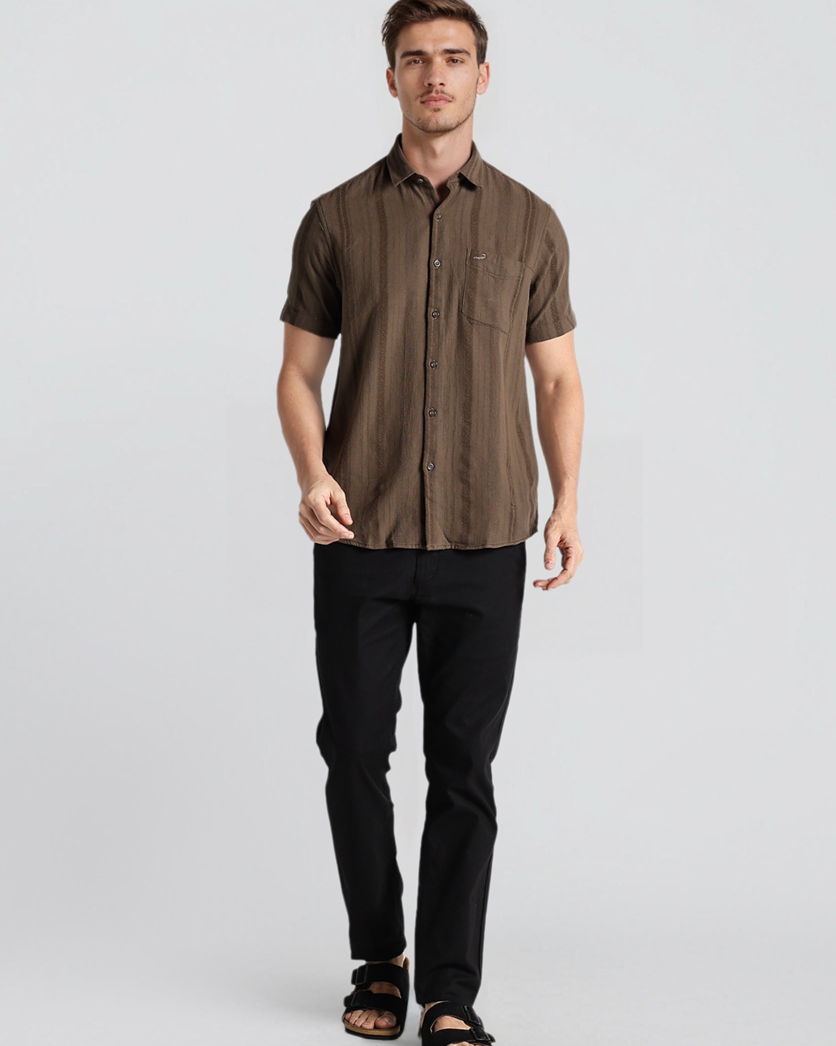 Man wearing a brown short-sleeve shirt and black pants on a light gray background