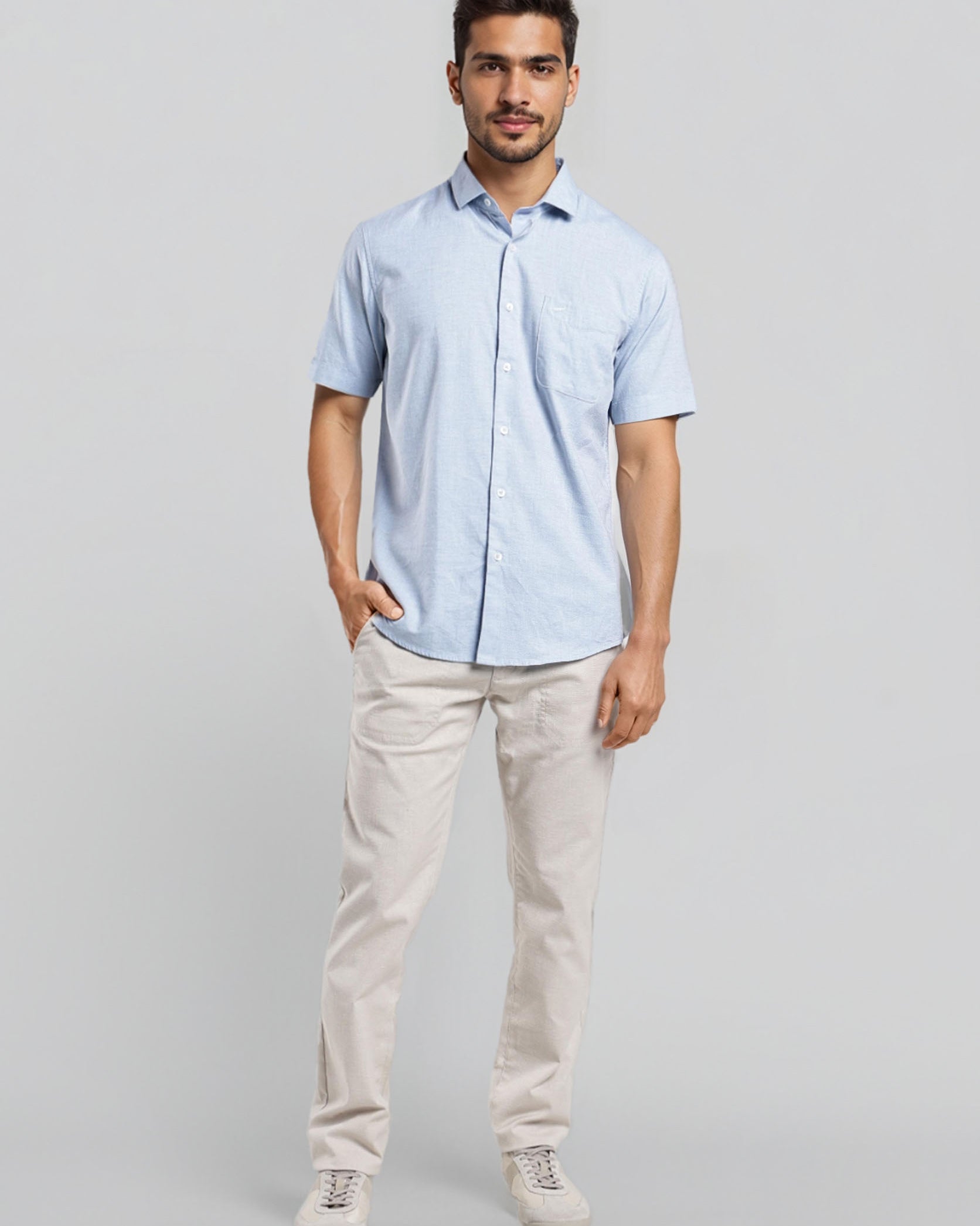 Man wearing a light blue shirt and beige pants on a gray background