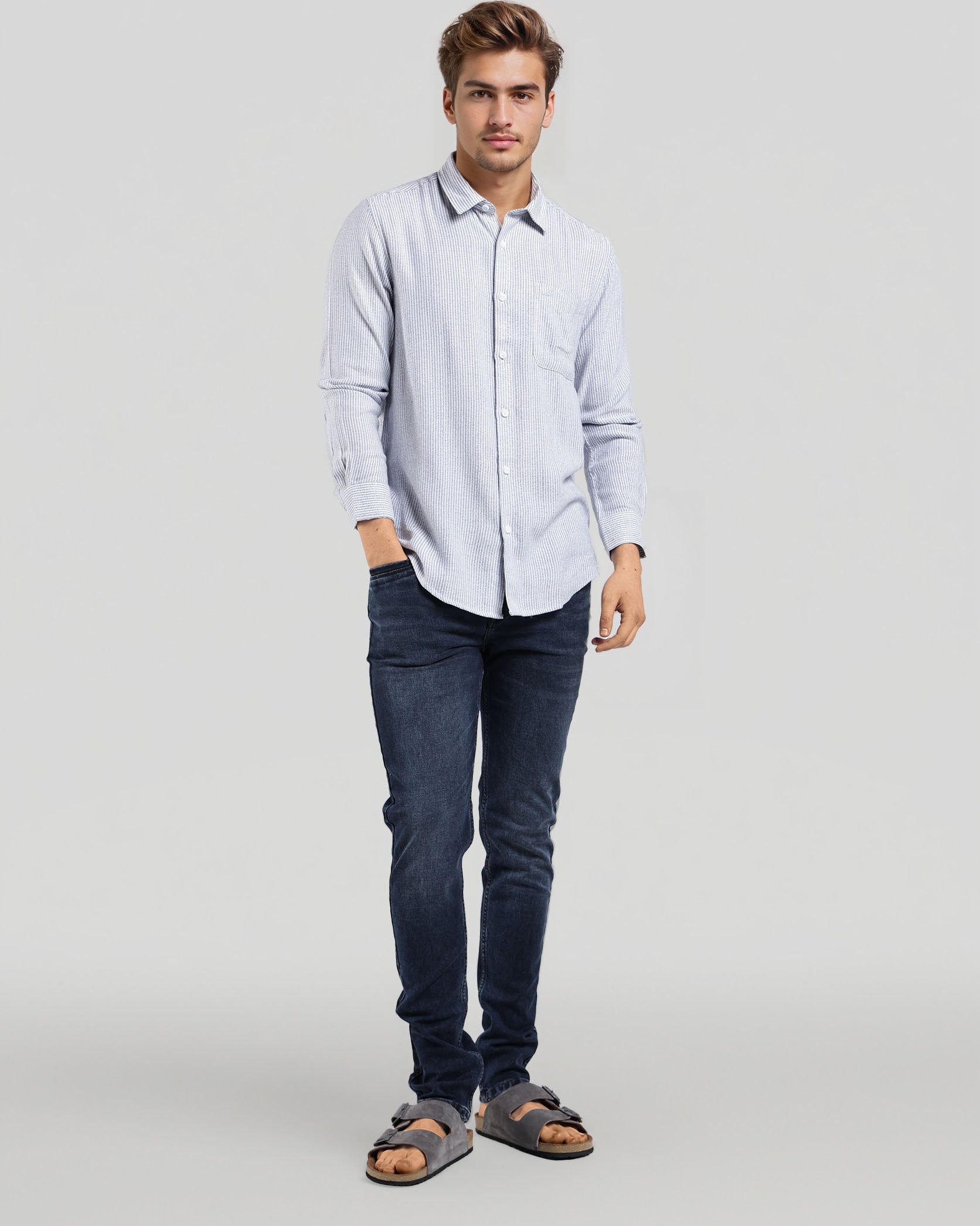 Man wearing a light blue shirt and dark jeans standing against a plain background