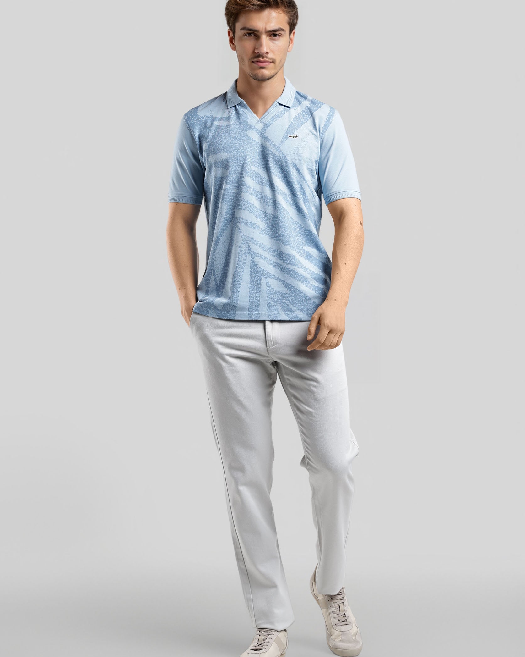 Man wearing a light blue striped polo shirt and white pants on a gray background