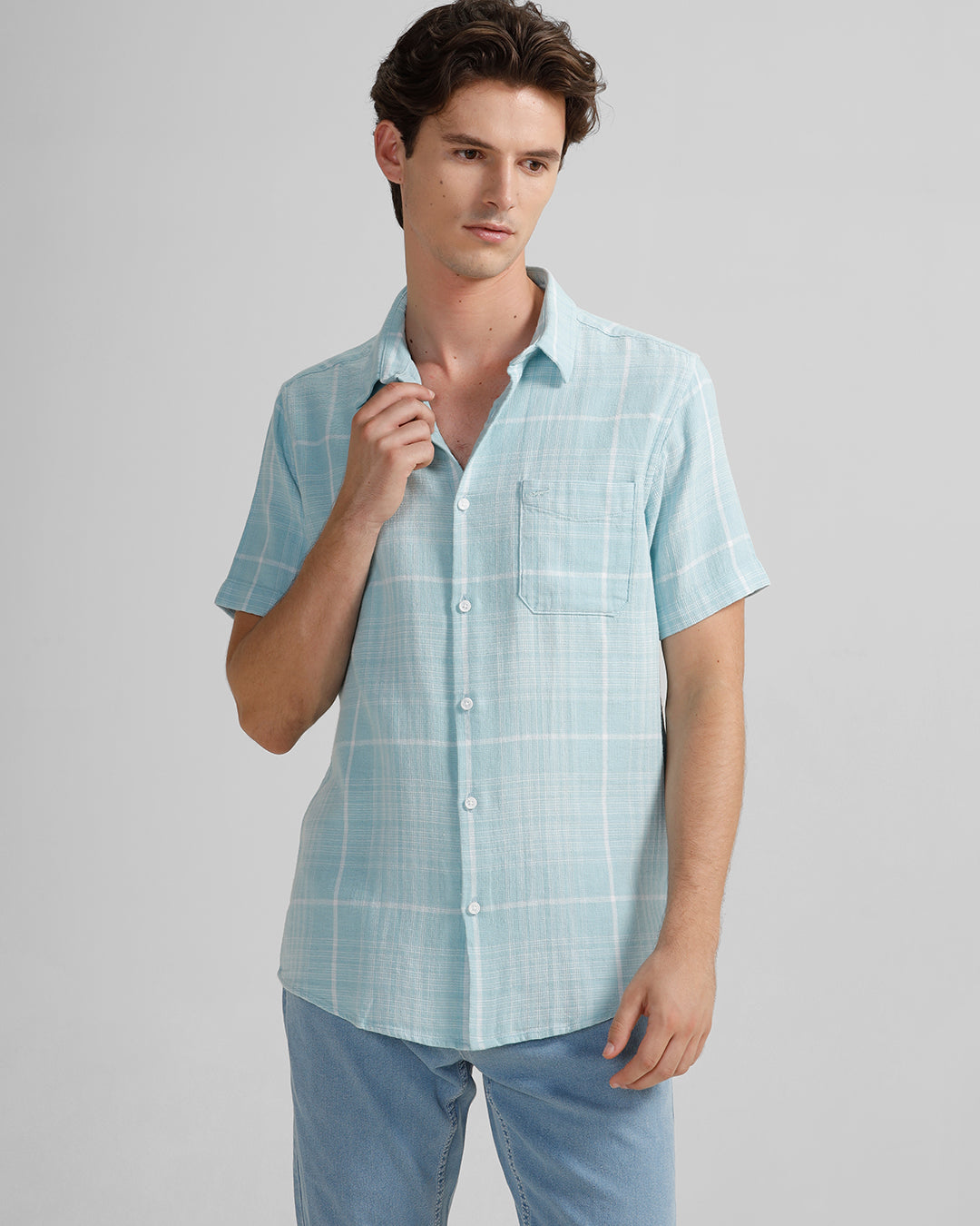 A man wearing a short-sleeved blue checked shirt with a collar and half sleeves, paired with light blue trousers.