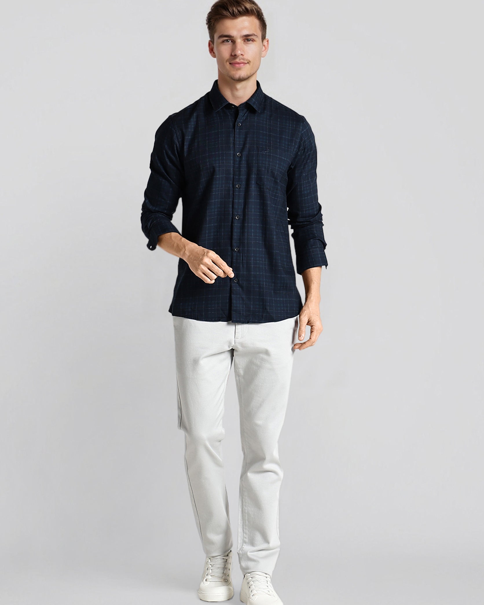 Man wearing a dark blue patterned shirt and white pants on a light gray background