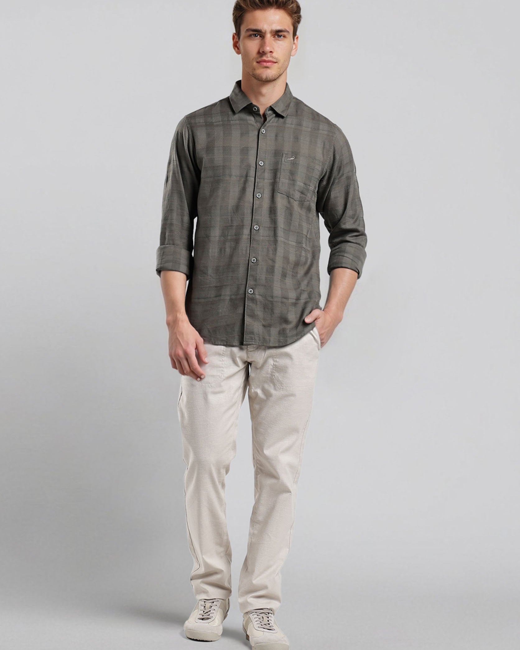 Man wearing a gray button-up shirt and beige pants on a light gray background