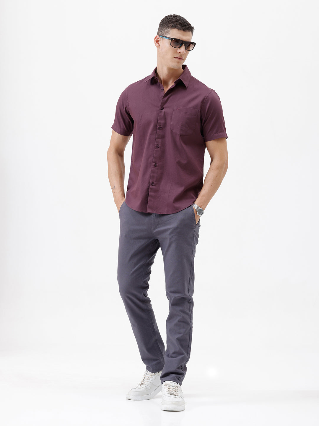 A man modeling a short-sleeve button-up shirt in a deep plum purple color, paired with gray trousers, against a plain white studio background.